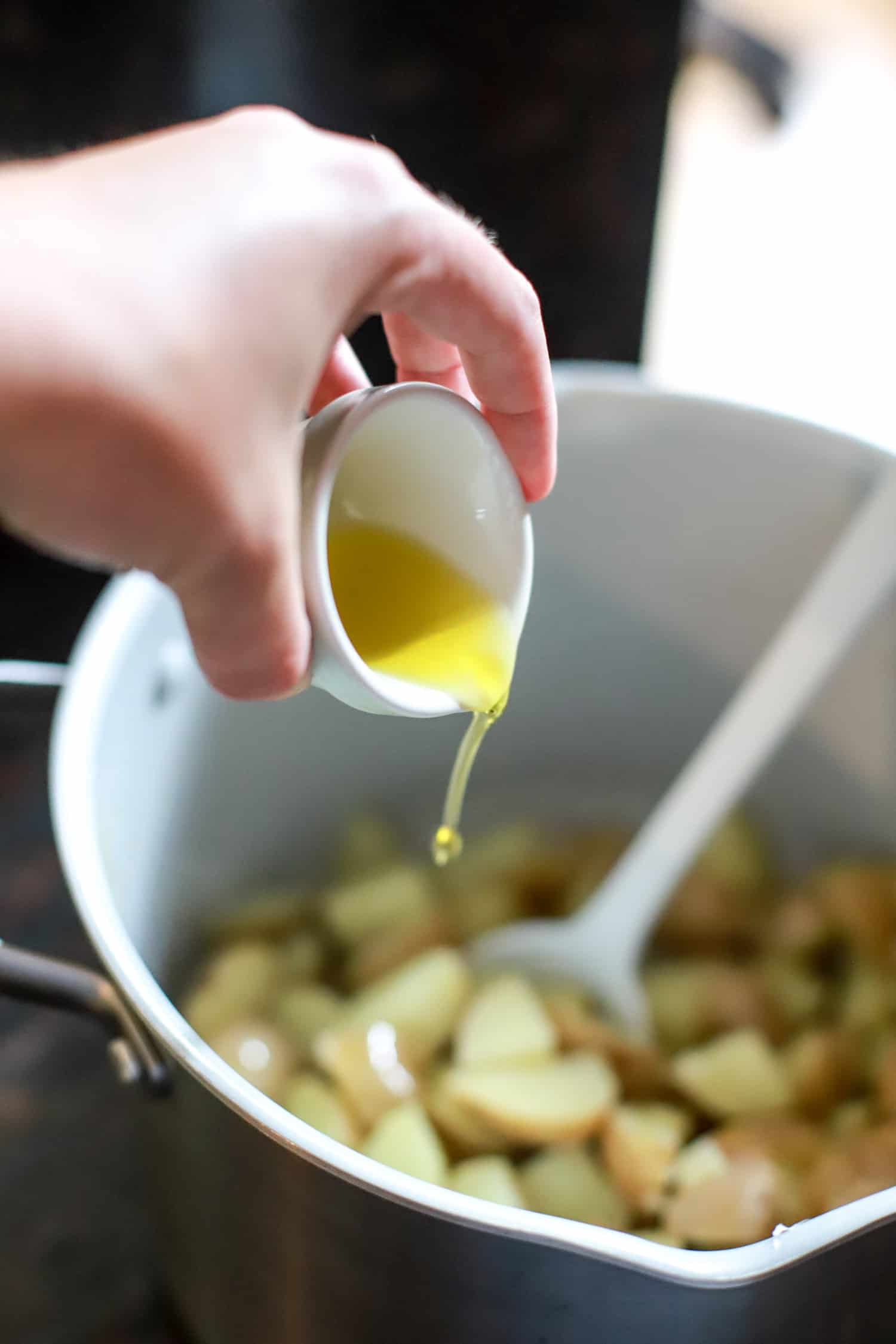 hand pouring olive oil over cooked potatoes