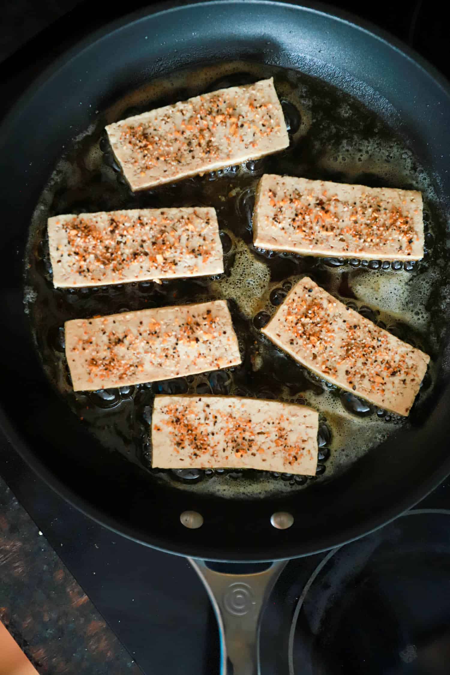 Black skillet with pieces of tofu frying.