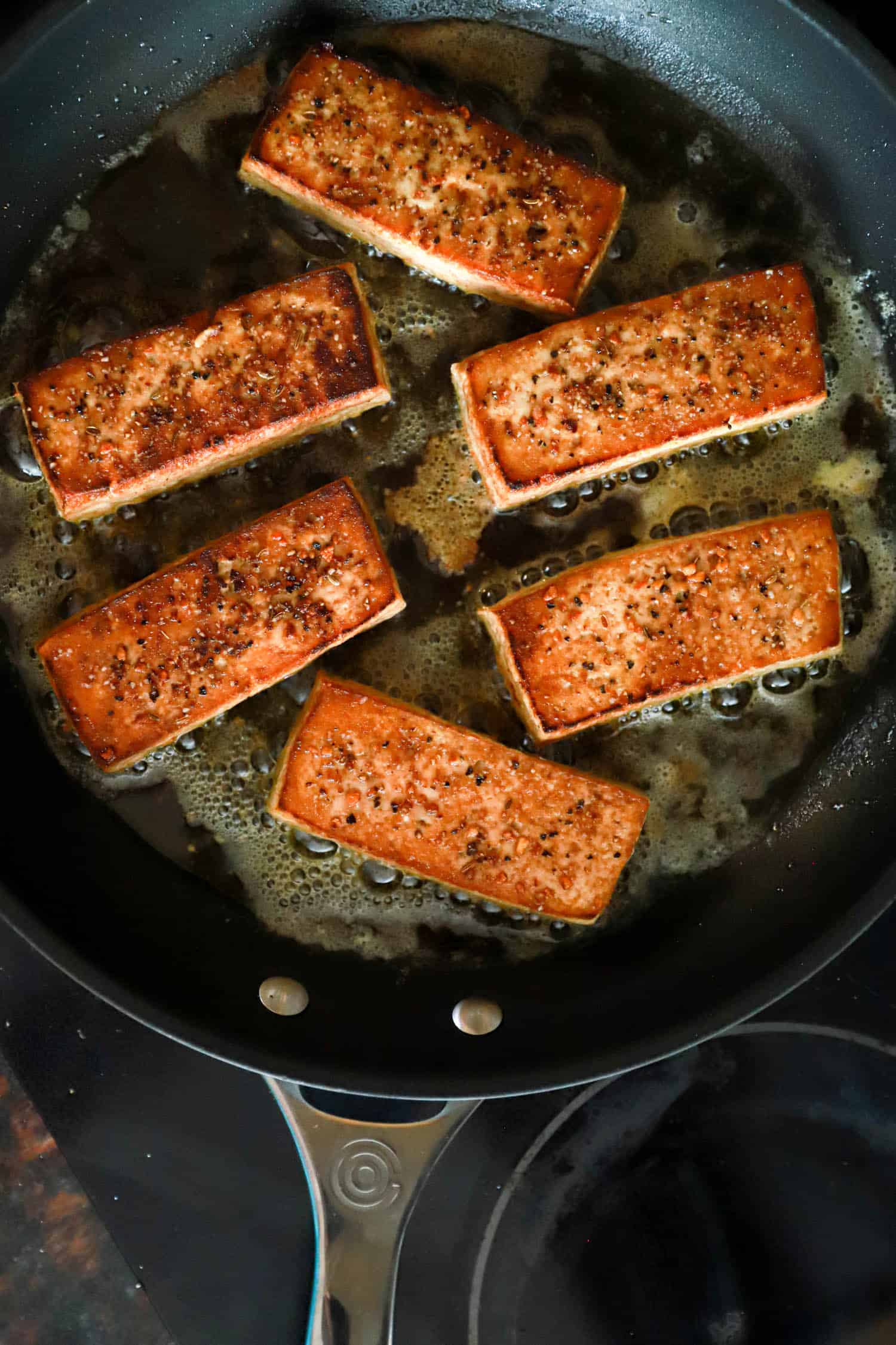 Golden brown tofu slabs in black nonstick skillet.