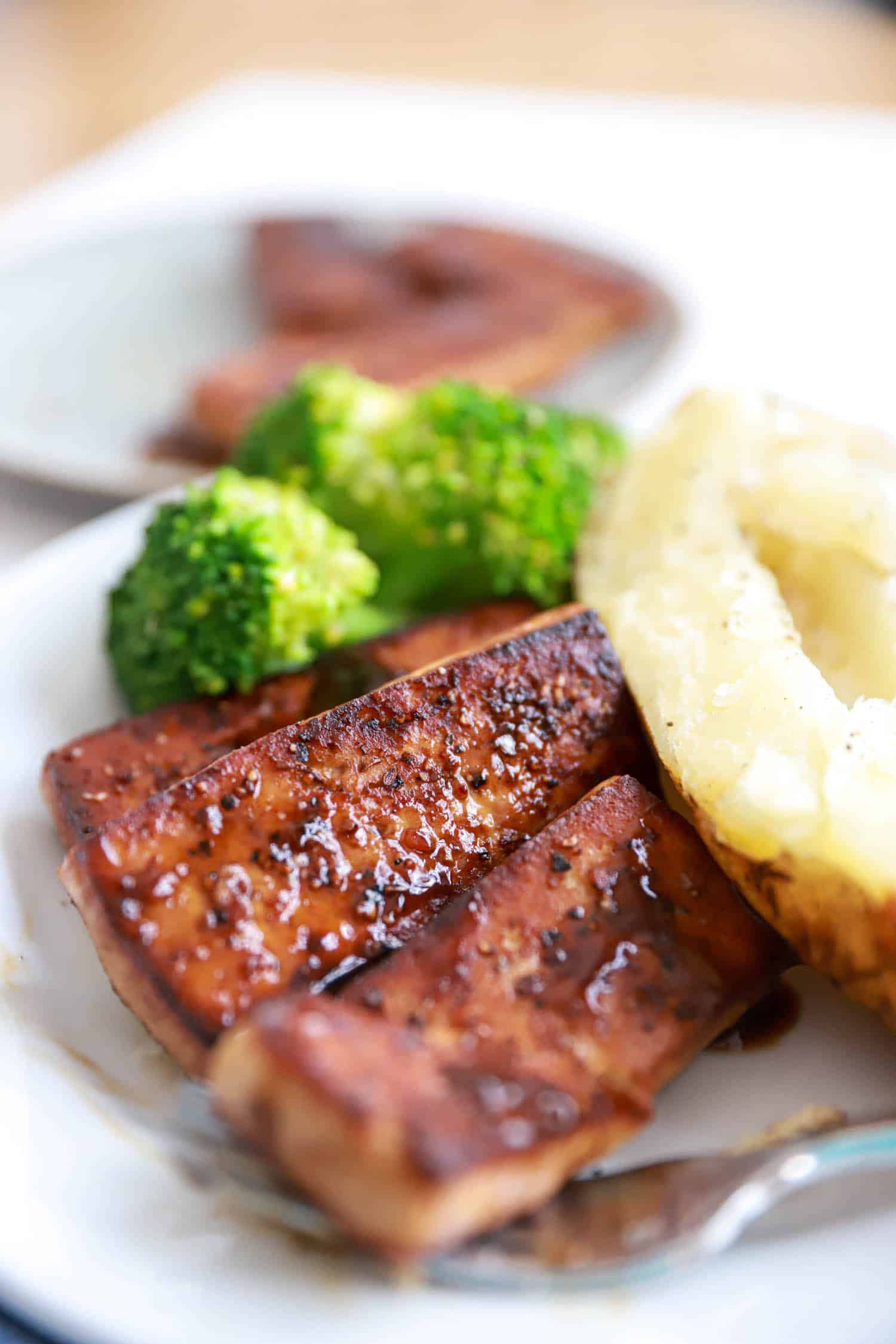 Side view of white plate with tofu steak and baked potato.