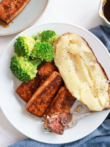 White plate with tofu steak, baked potato and steamed broccoli.