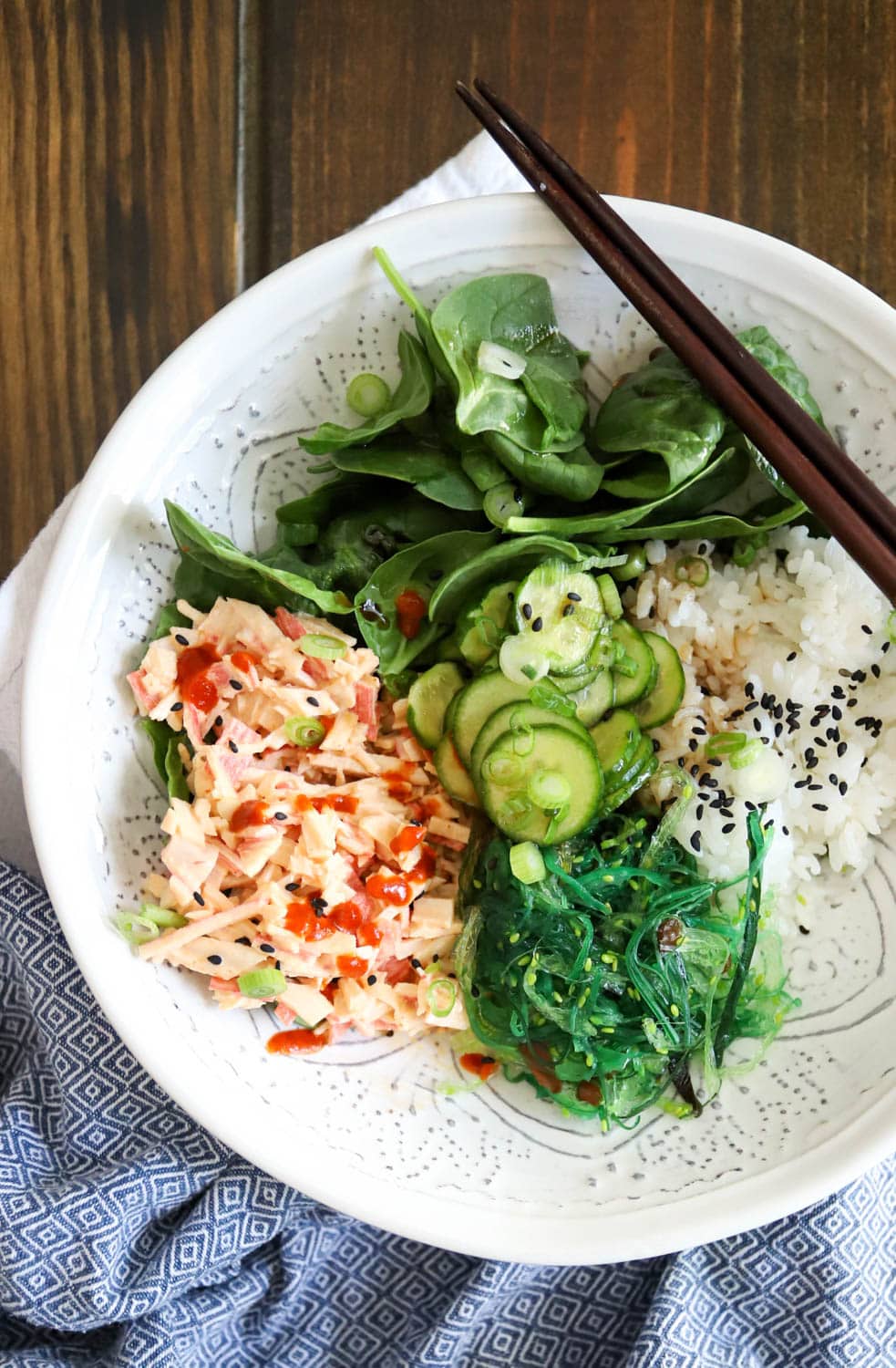 white bowl with spicy kani salad, greens, and seaweed salad over rice.