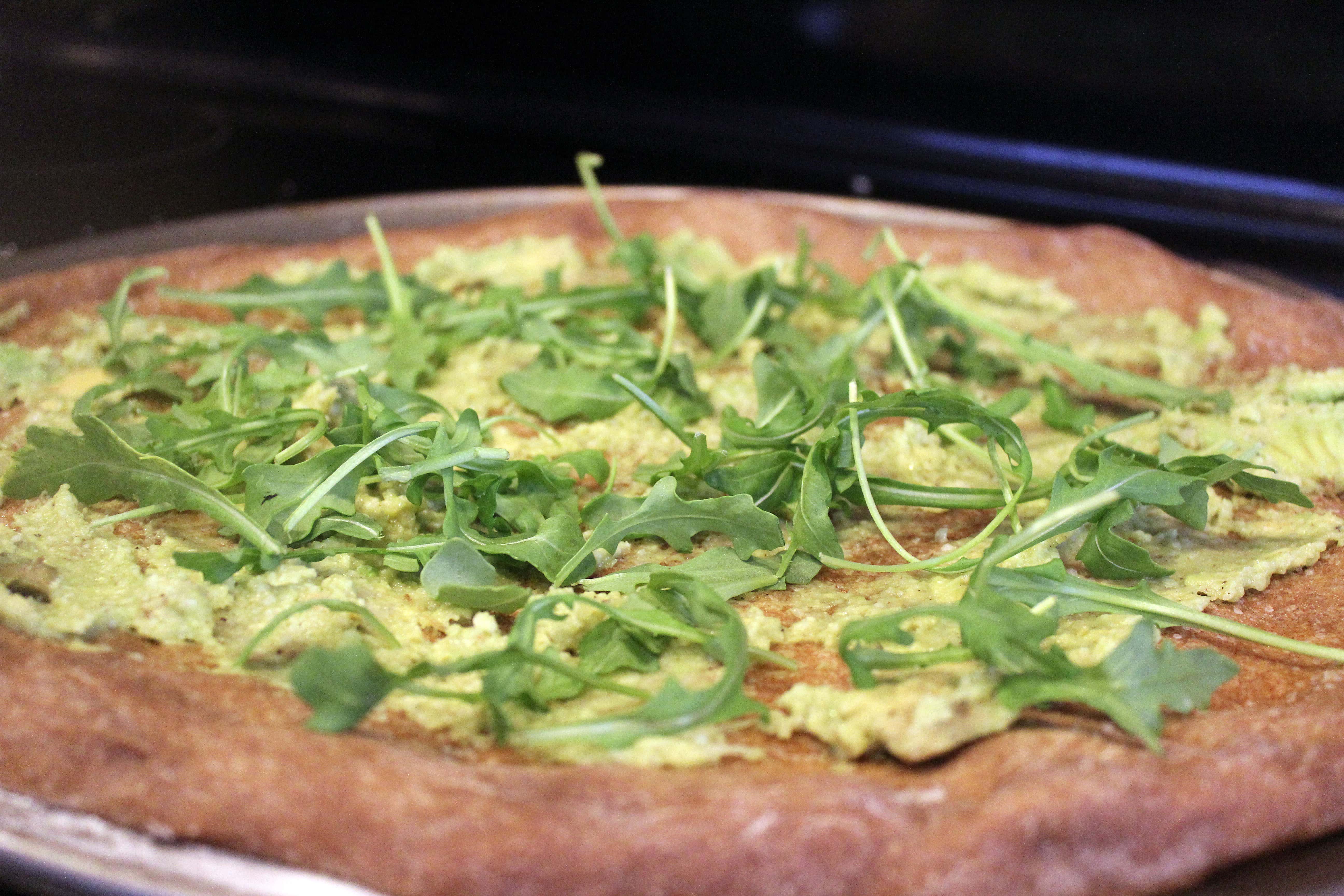Spread sauce on pizza and top with arugula