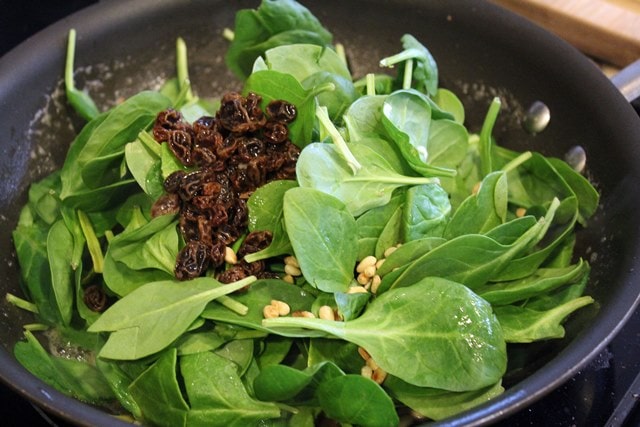 Add spinach, raisins, and pine nuts to wilt