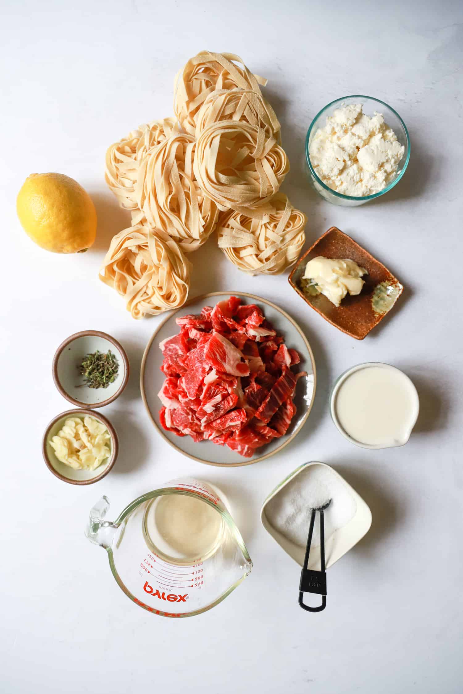 ingredients for sliced steak pasta on white board.