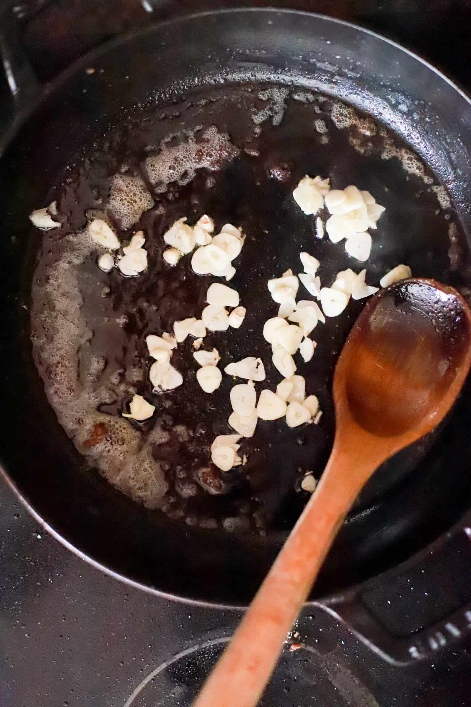 Large black pan with sliced garlic in steak drippings.