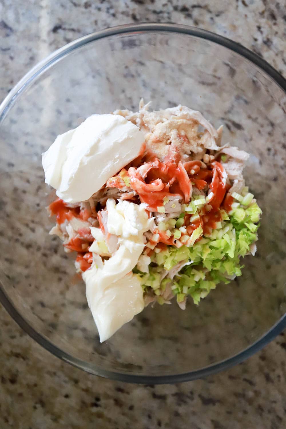 Glass bowl with ingredients for buffalo chicken dip finely chopped.