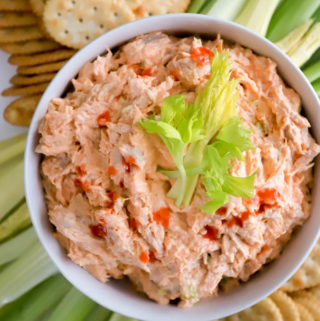 cold buffalo chicken salad in white bowl with celery leaves on top.