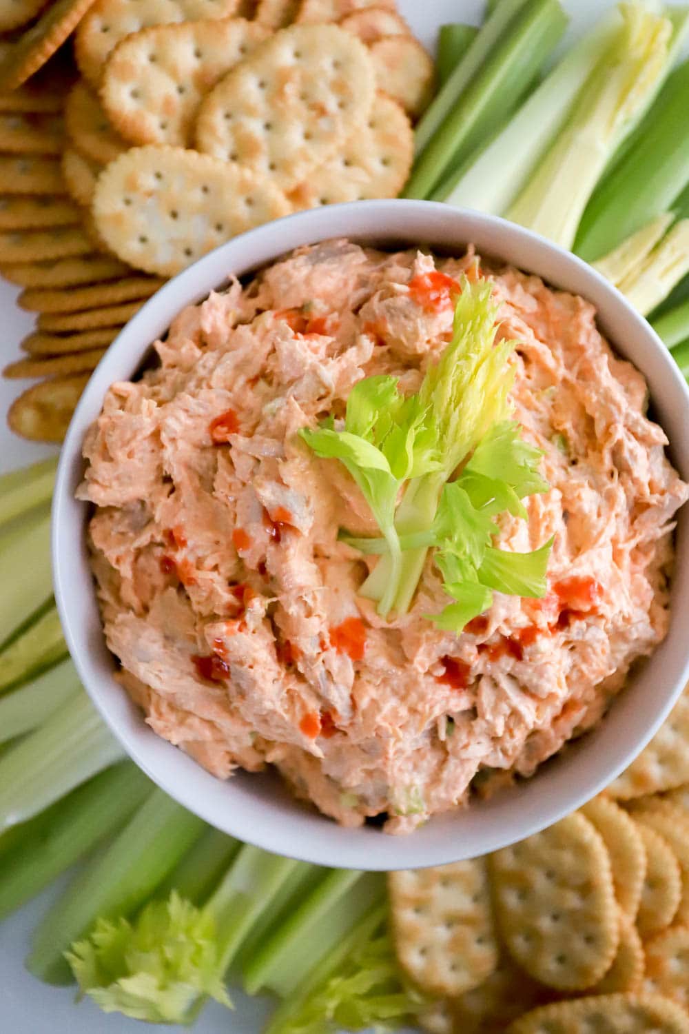 cold buffalo chicken salad in white bowl with celery leaves on top.