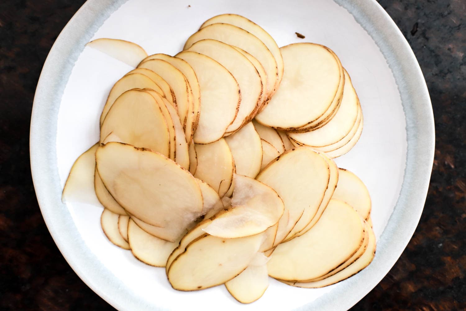 mandonline sliced russet potatoes on white plate.