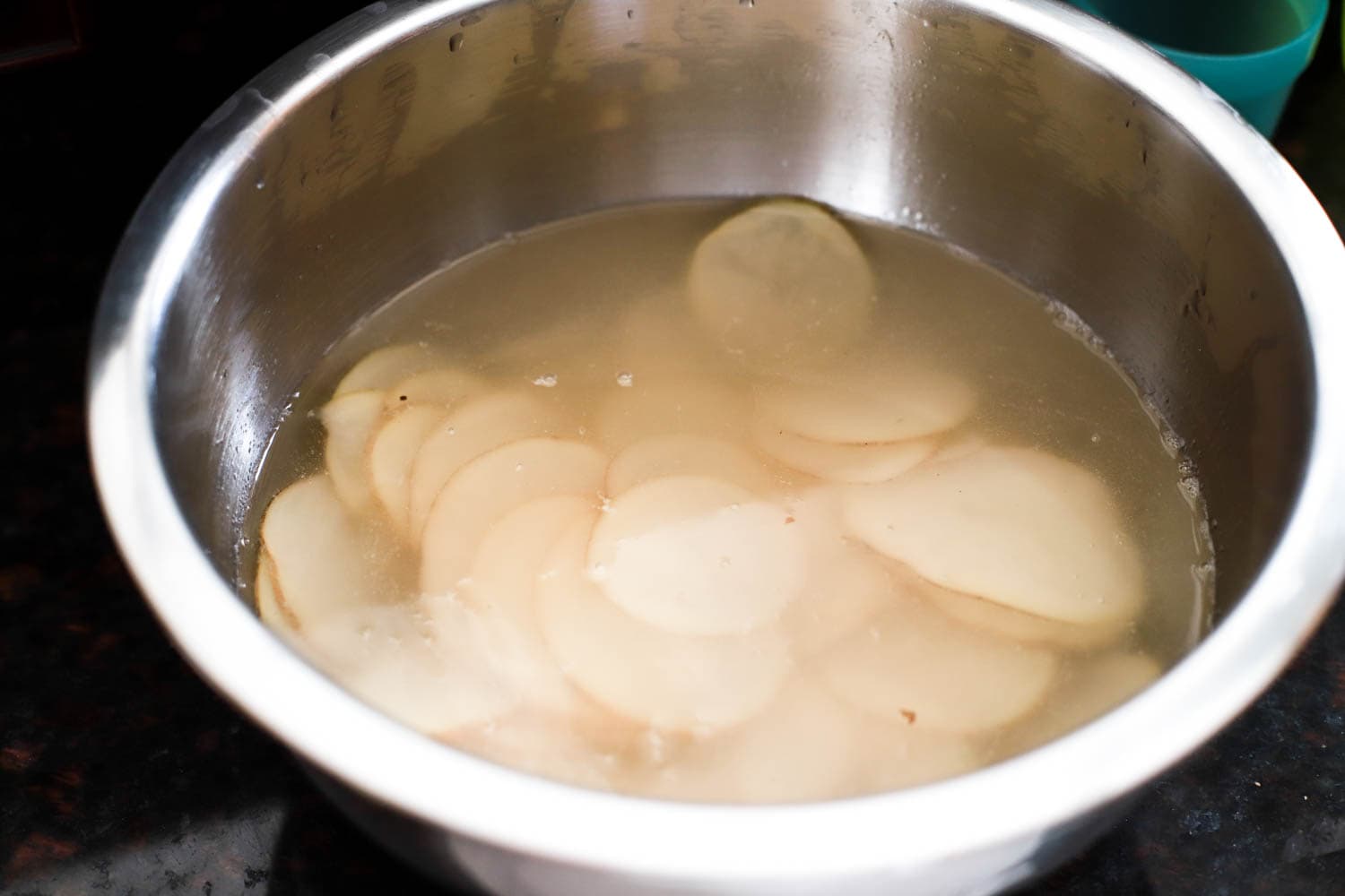 mandonline sliced russet potatoes soaking in bowl of water.
