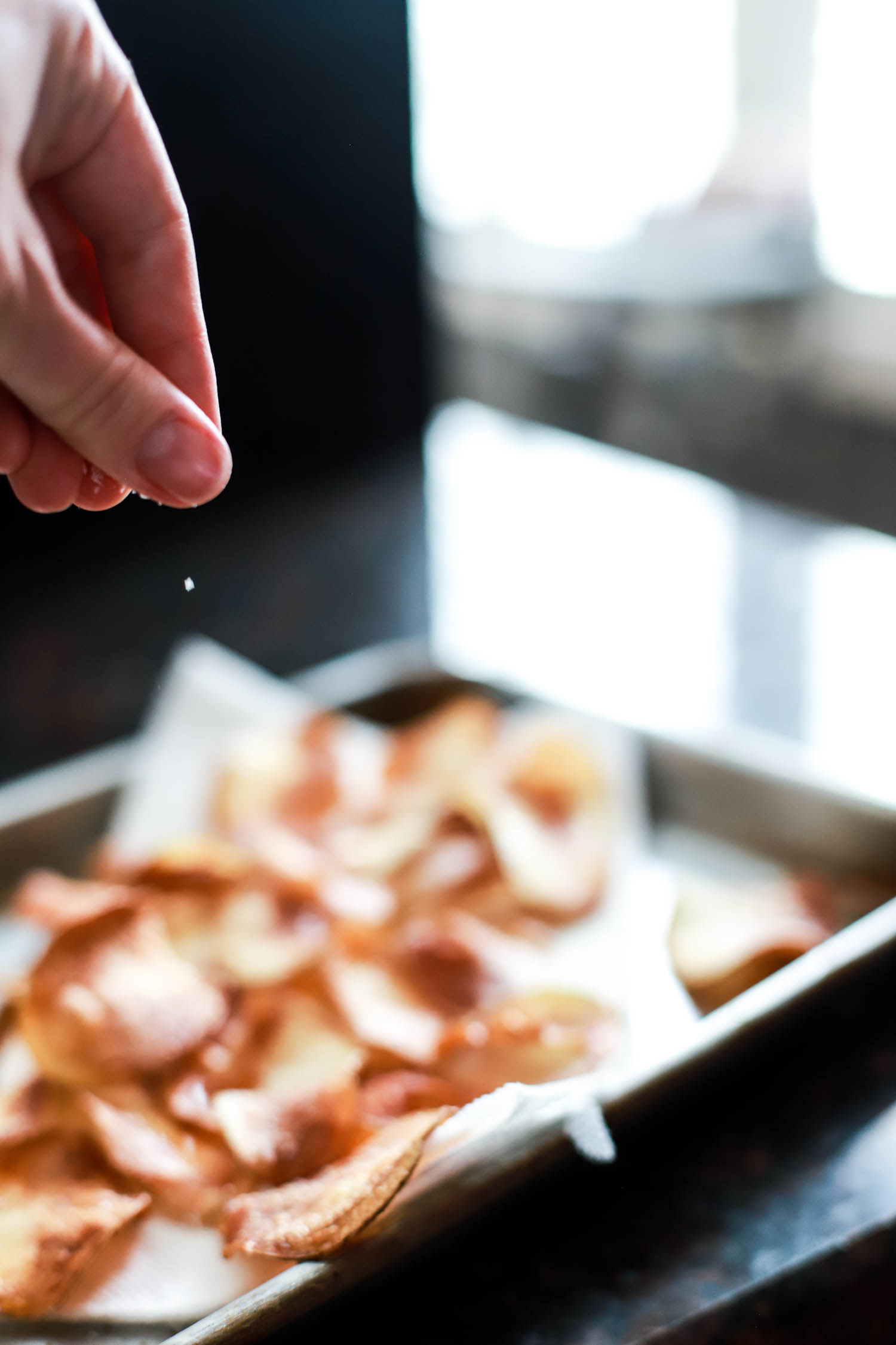 hand sprinkling freshly fried potato chips with kosher salt.