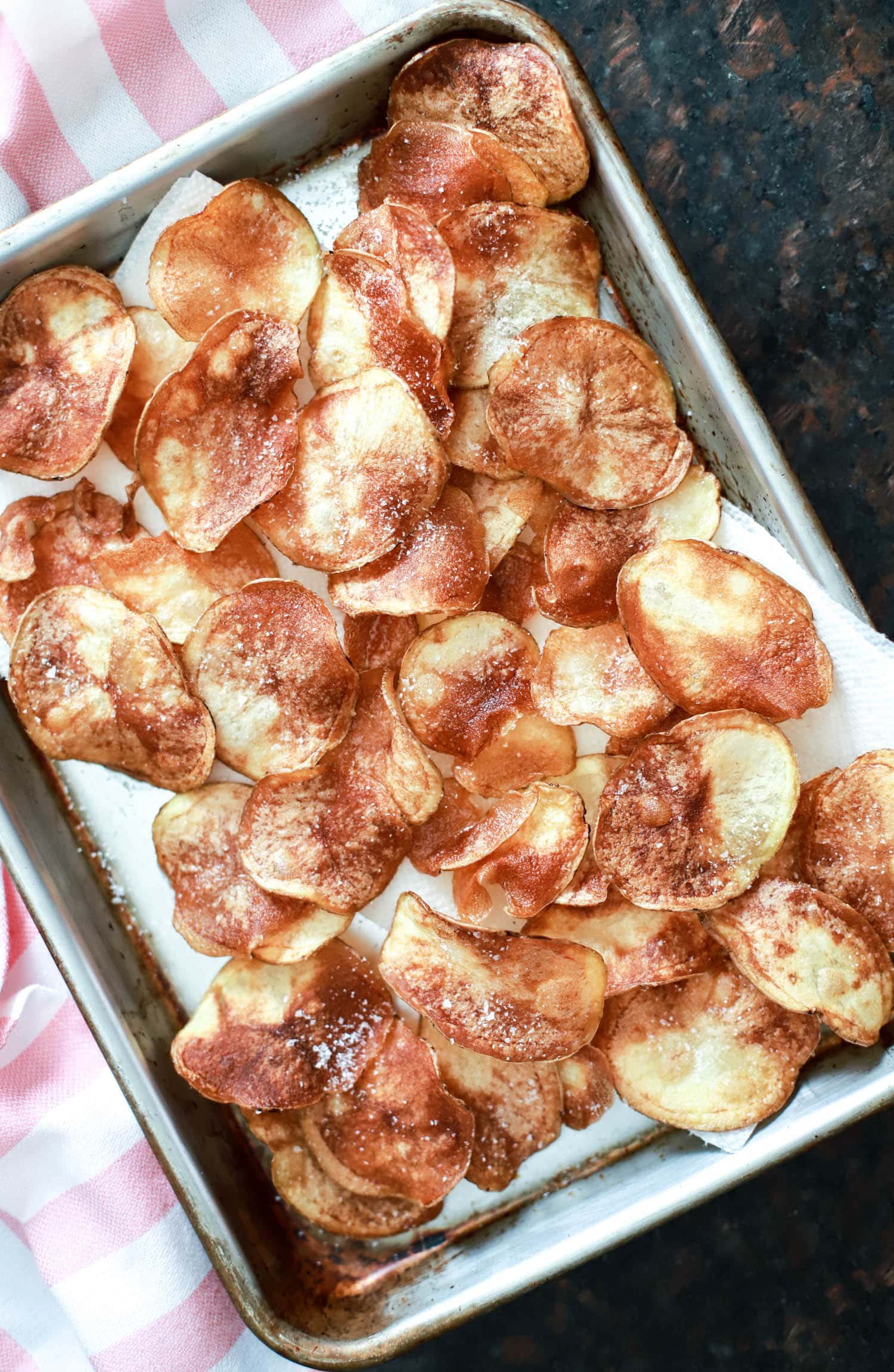 homemade potato chips on a baking sheet with kosher salt.