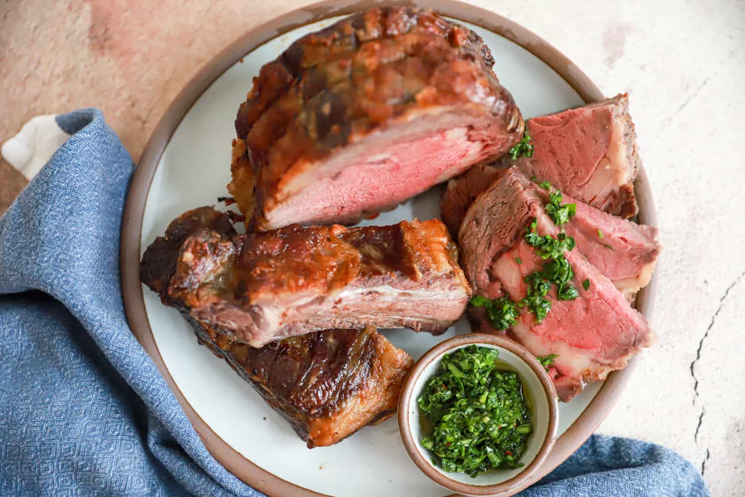 sliced prime rib with sauce for prime rib and roasted rib bones on round plate.