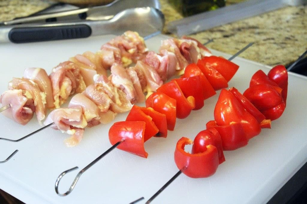 skewers with bell pepper chunks and chicken thigh pieces on white cutting board.