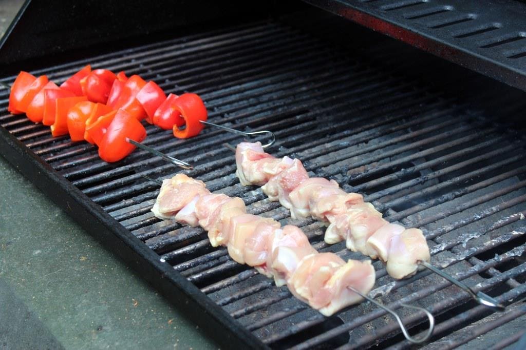 hibachi chicken skewers and skewers of red bell peppers on a grill.