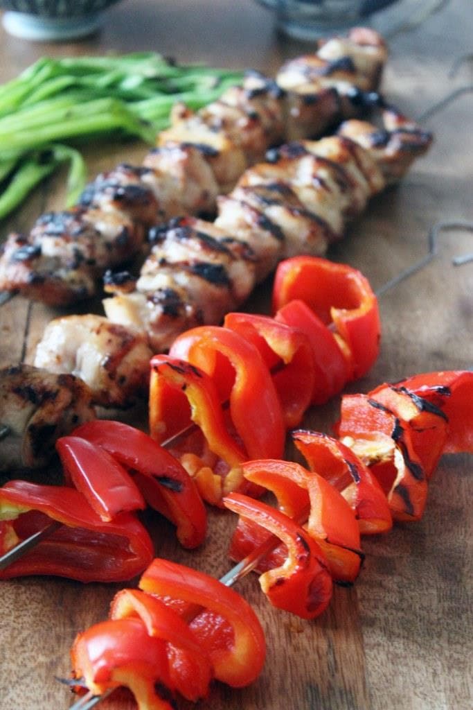 close up of grilled red bell pepper skewers with hibachi style chicken skewers in the background.