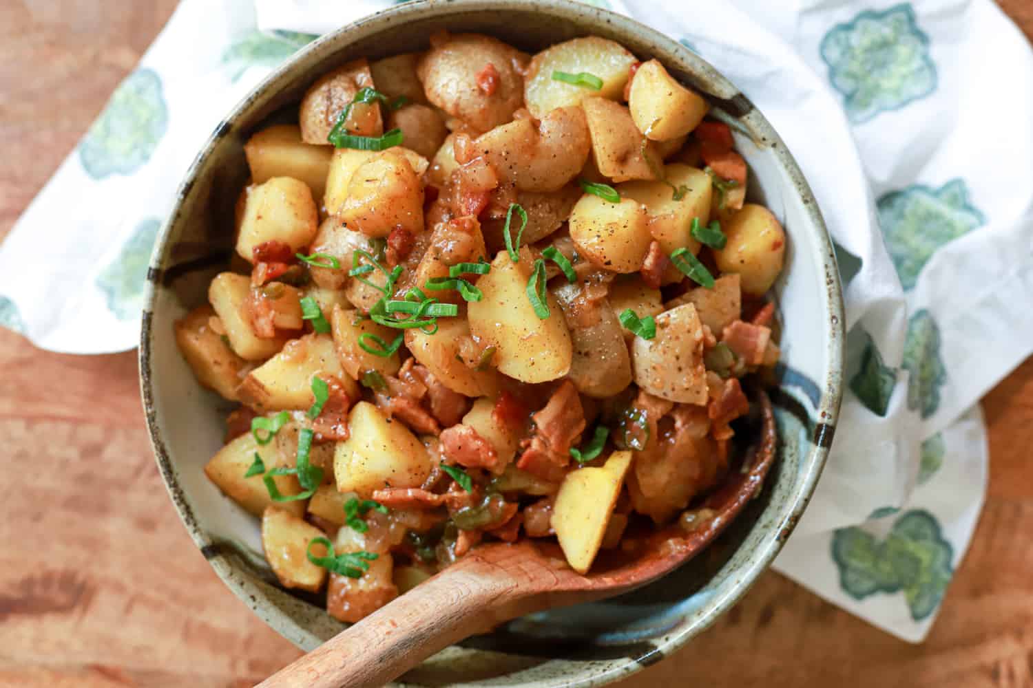 Round ceramic bowl of german potato salad with wooden spoon.