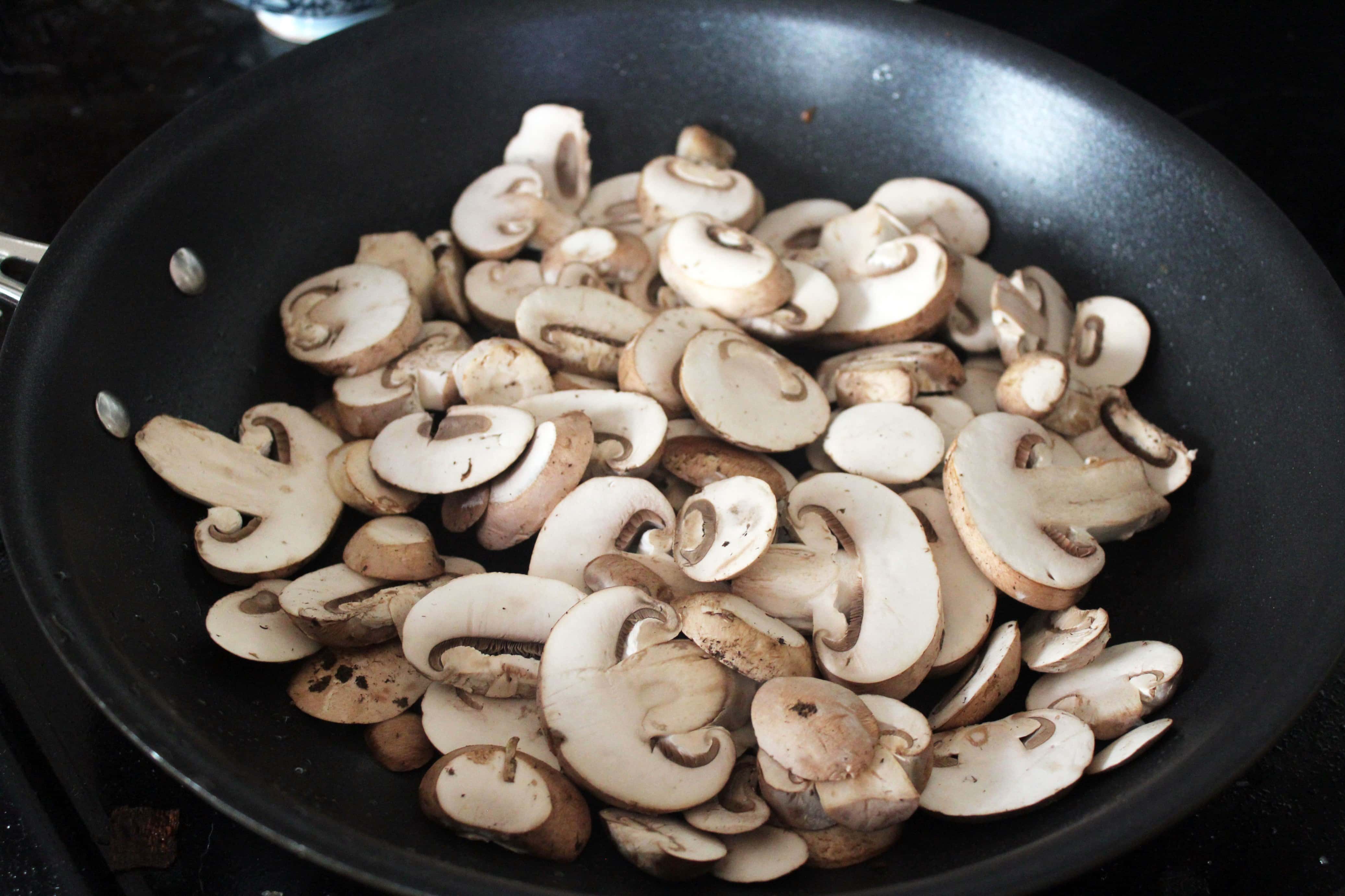 skillet of raw mushrooms being cooked down for casserole.