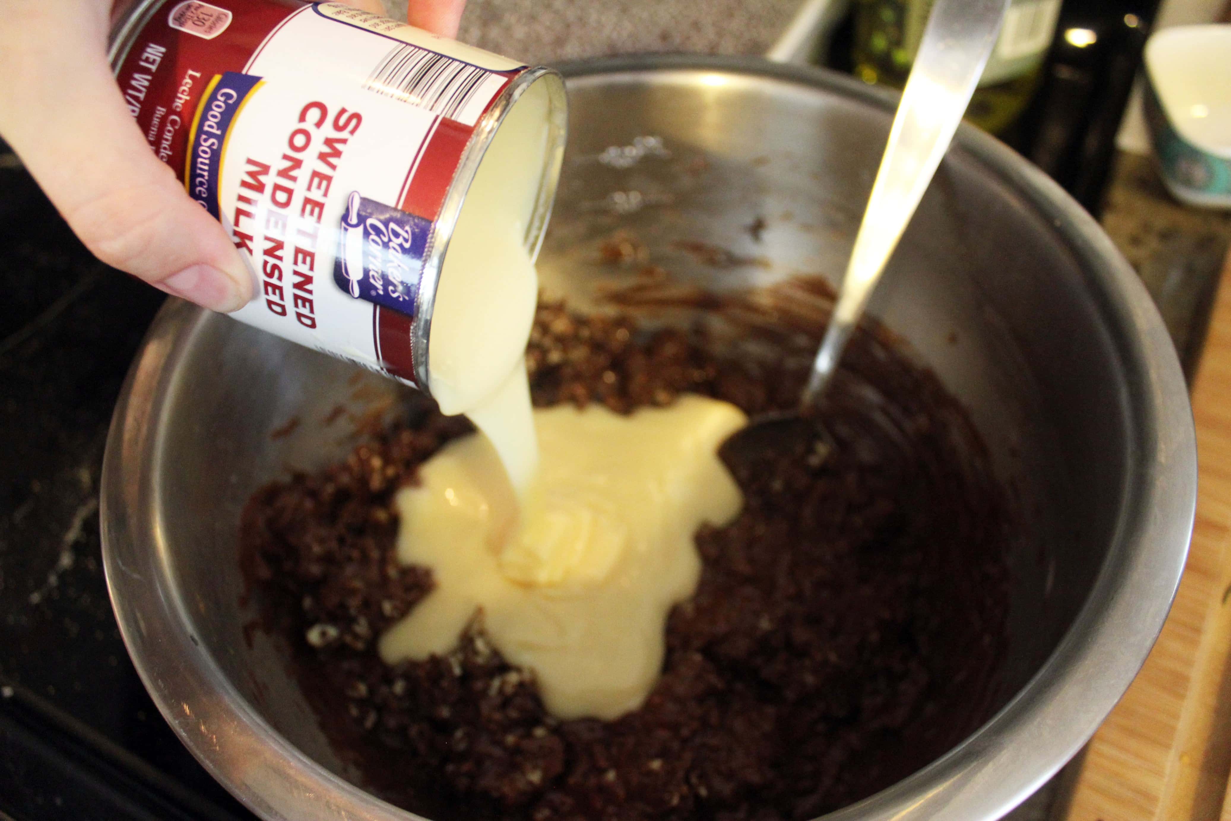 hand pouring sweetened condensed milk into a bowl of chocolate chips for fudge.