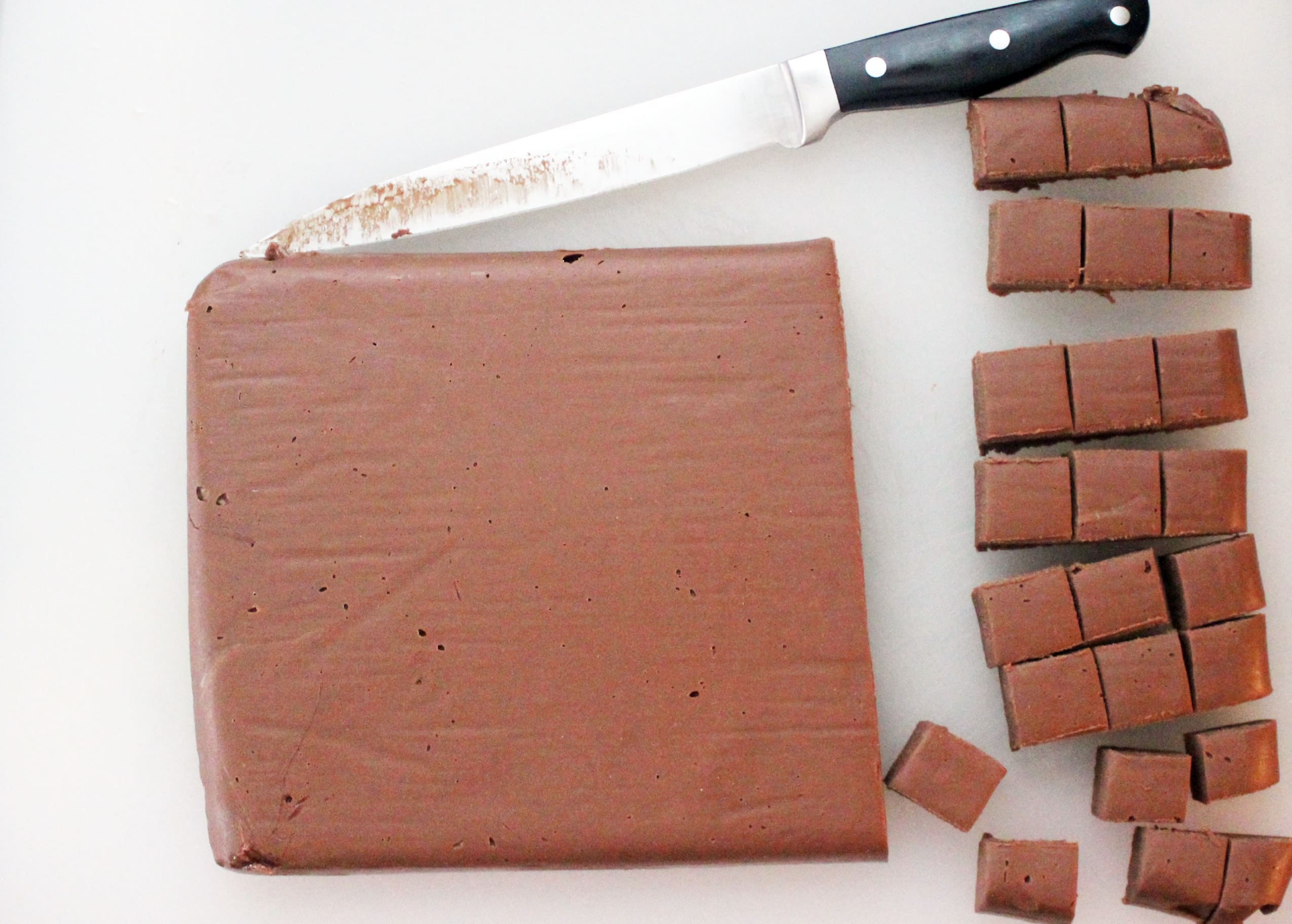 white cutting board with knife cutting fudge into small cubes.