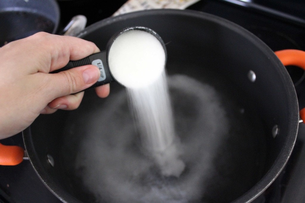 hand pouring sugar into a pot of water