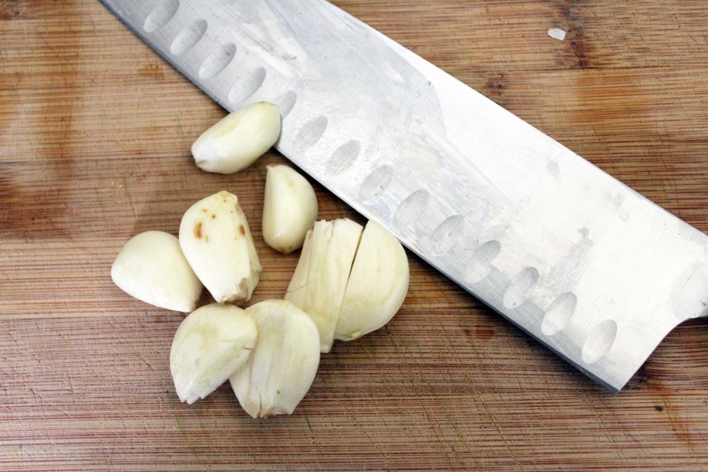 garlic cloves with knife on cutting board