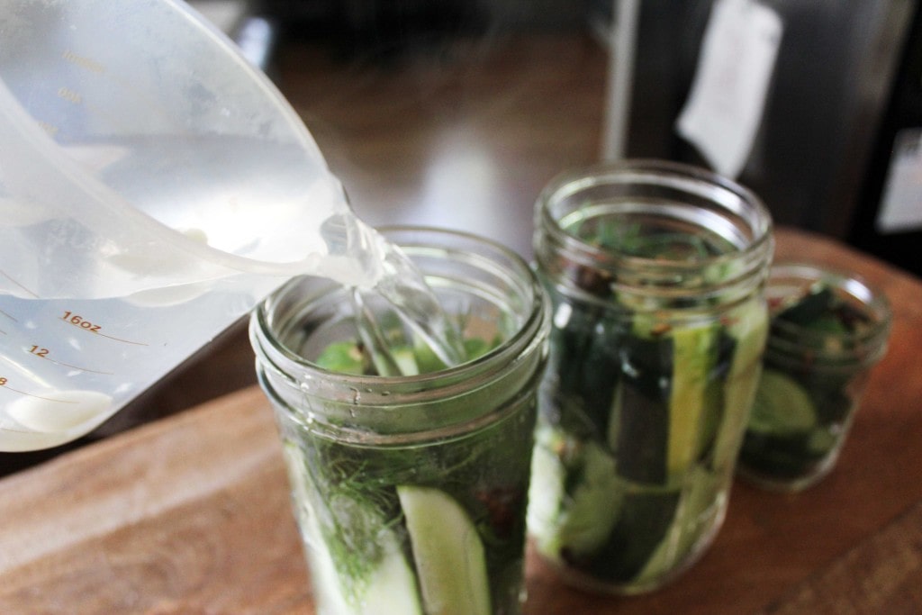 liquid being poured into jars for pickles with cucumbers