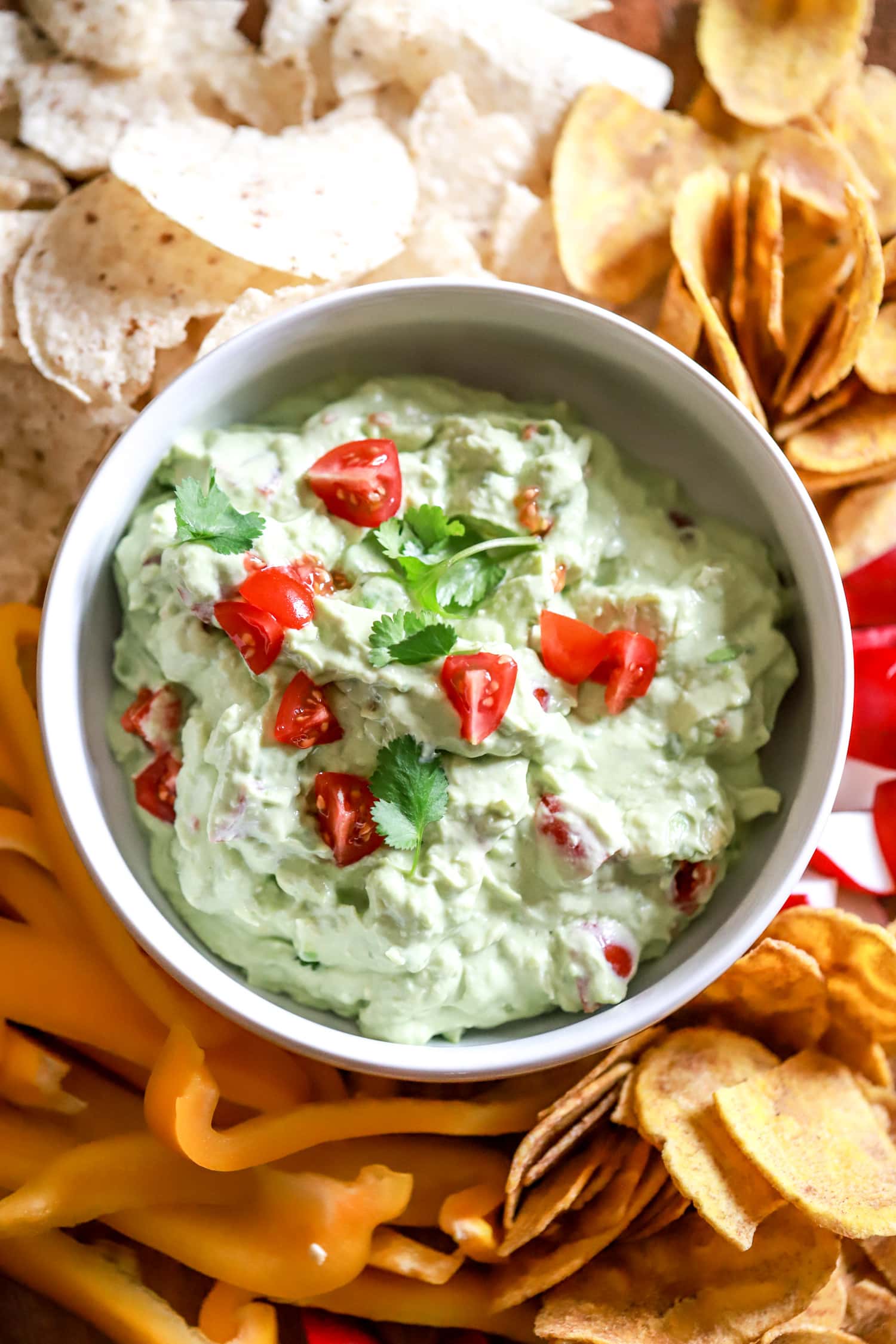bowl of homemade sour cream guacamole surrounded by peppers and plaintain chips for dipping.