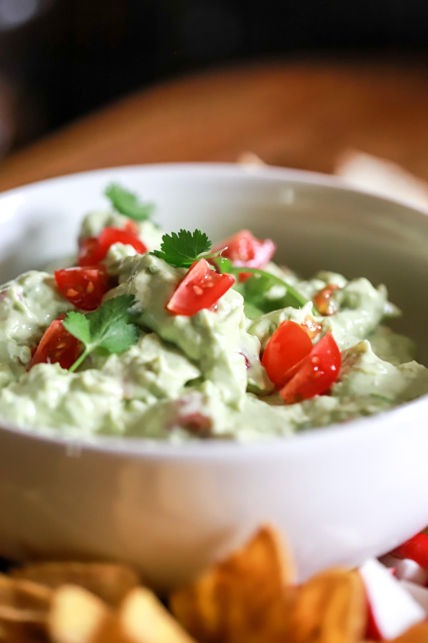 bowl of sour cream guacamole side view topped with tomatoes and cilantro.