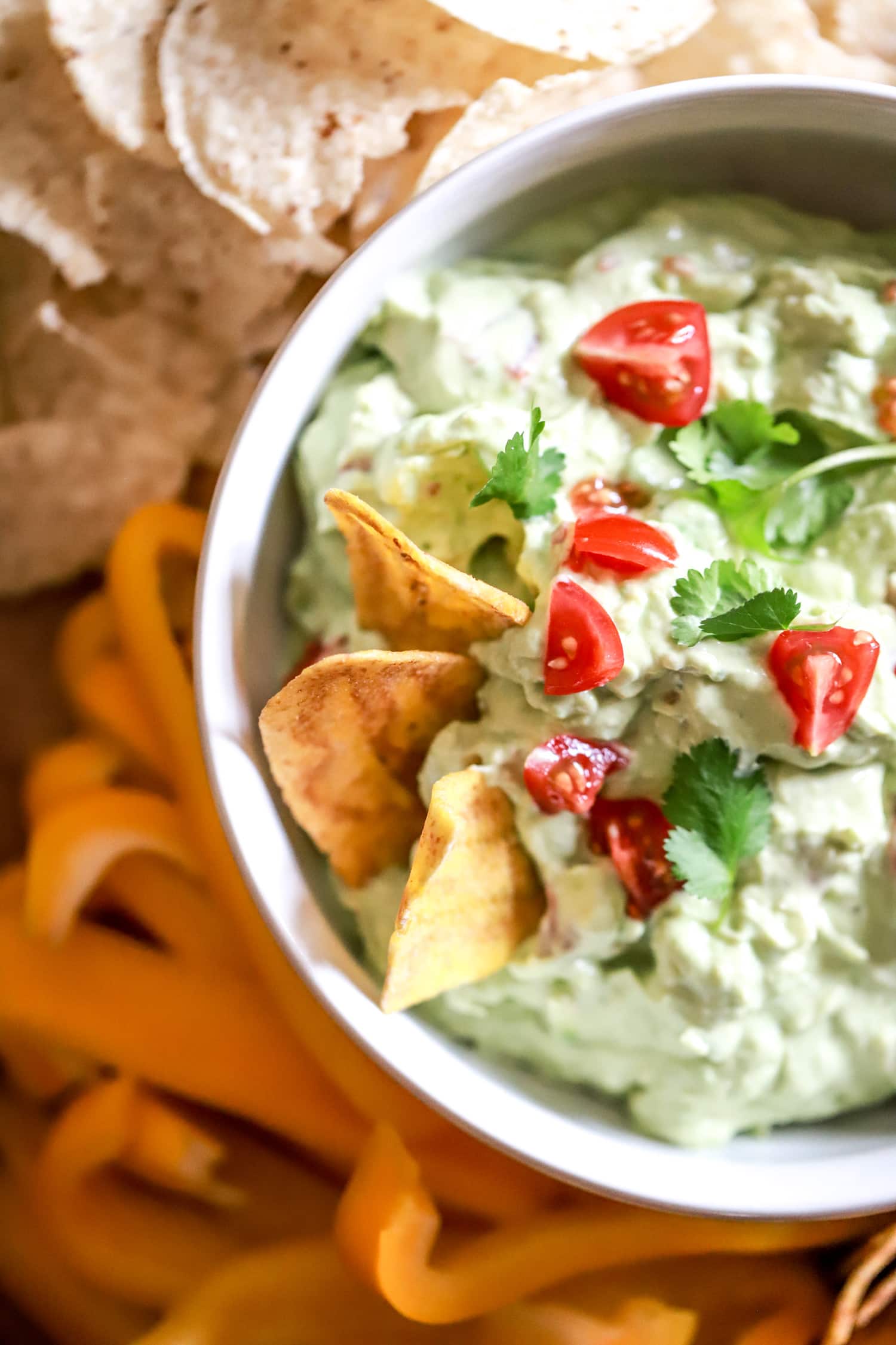 plantain chips in bowl of creamy guacamole topped with tomatoes and cilantro.