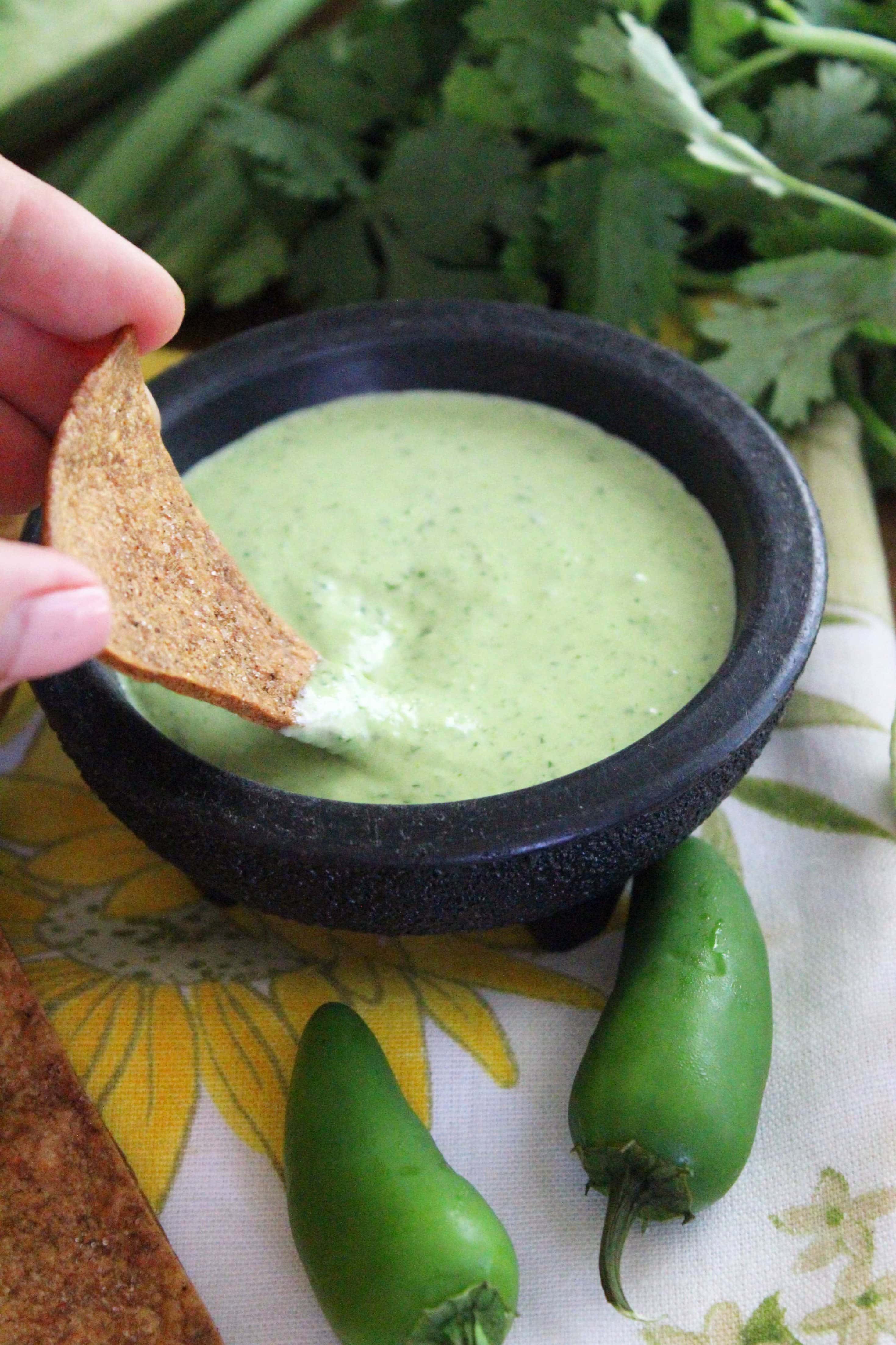 hand dipping chip into green spicy ranch dressing.