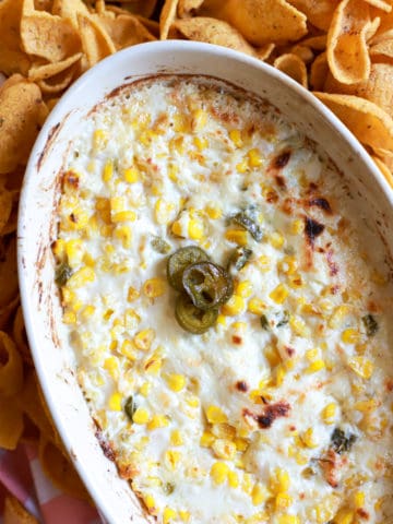 oval baking dish with cheesy corn dip topped with pickled jalapenos.