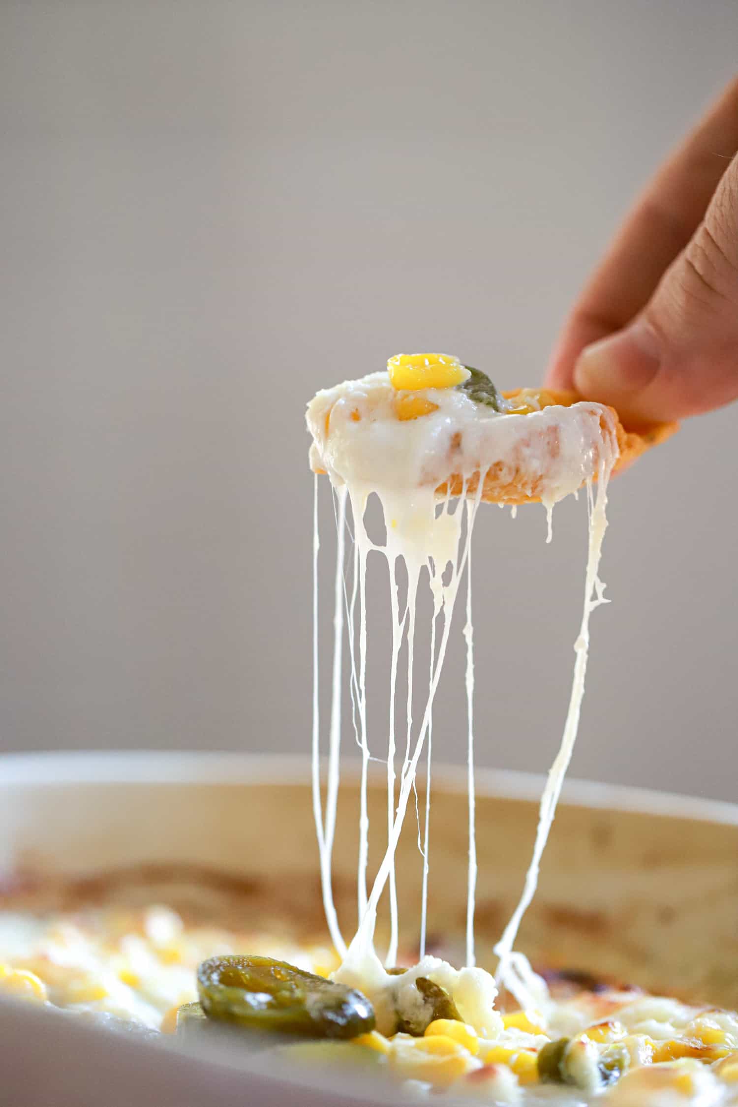 hand scooping cheesy corn dip in air on white background.
