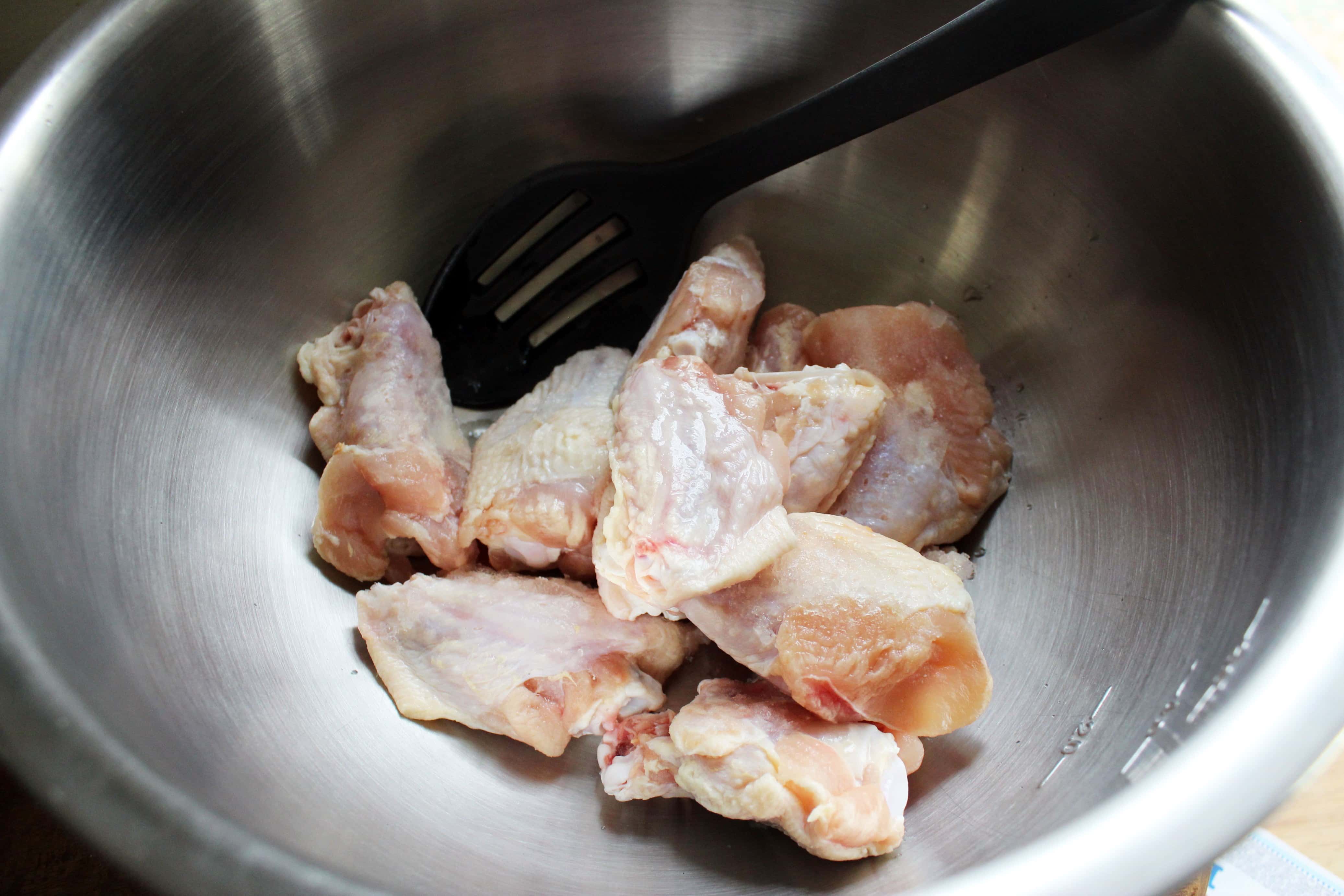 stainless steel bowl with raw chicken wing pieces.