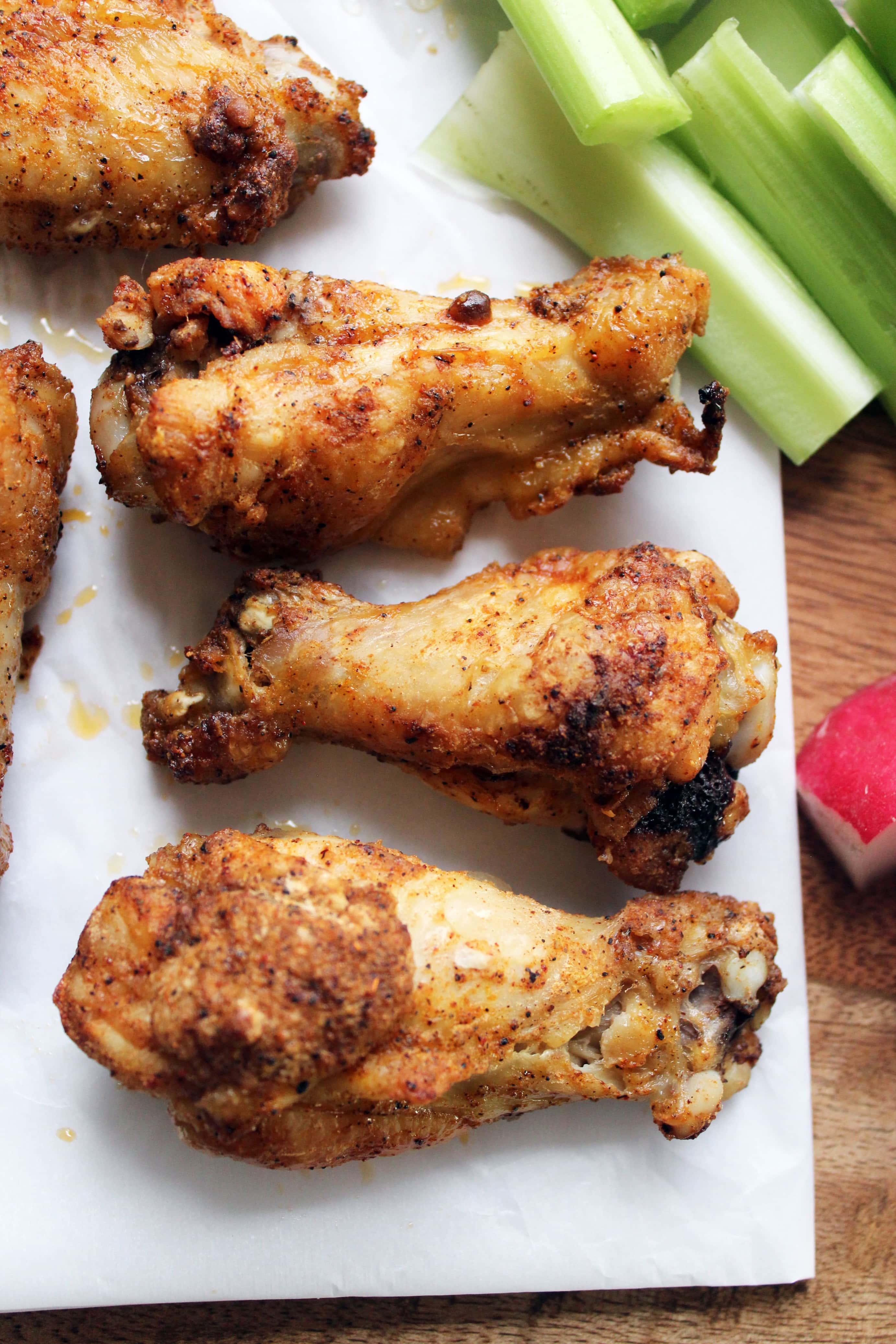 three baked chicken wings in a row on white parchment paper with celery sticks on the side.