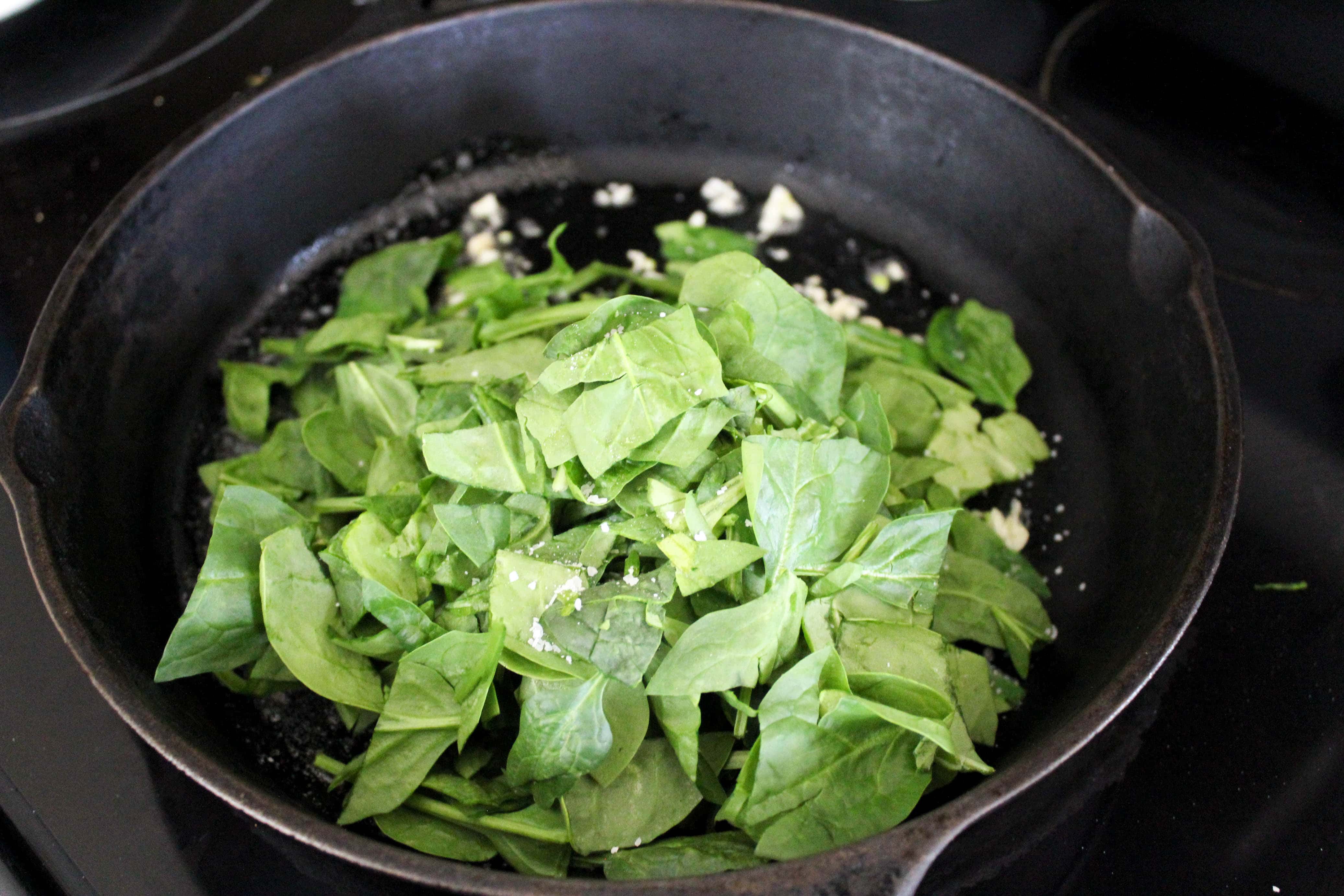 Chopped spinach being wilted in a black cast iron skillet.