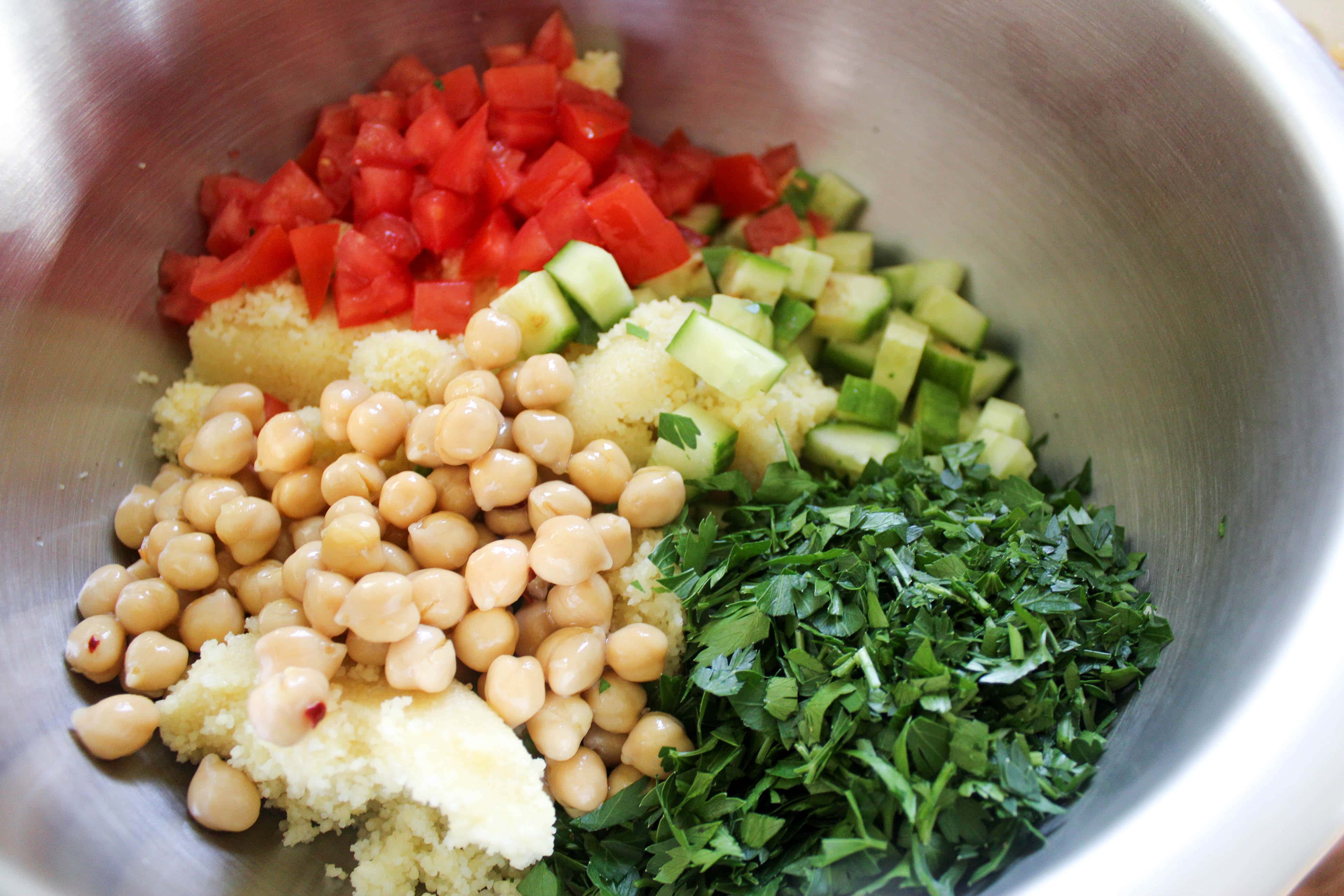 metal mixing bowl with couscous, parsley, and cucumbers with garbanzo beans for tabouli salad