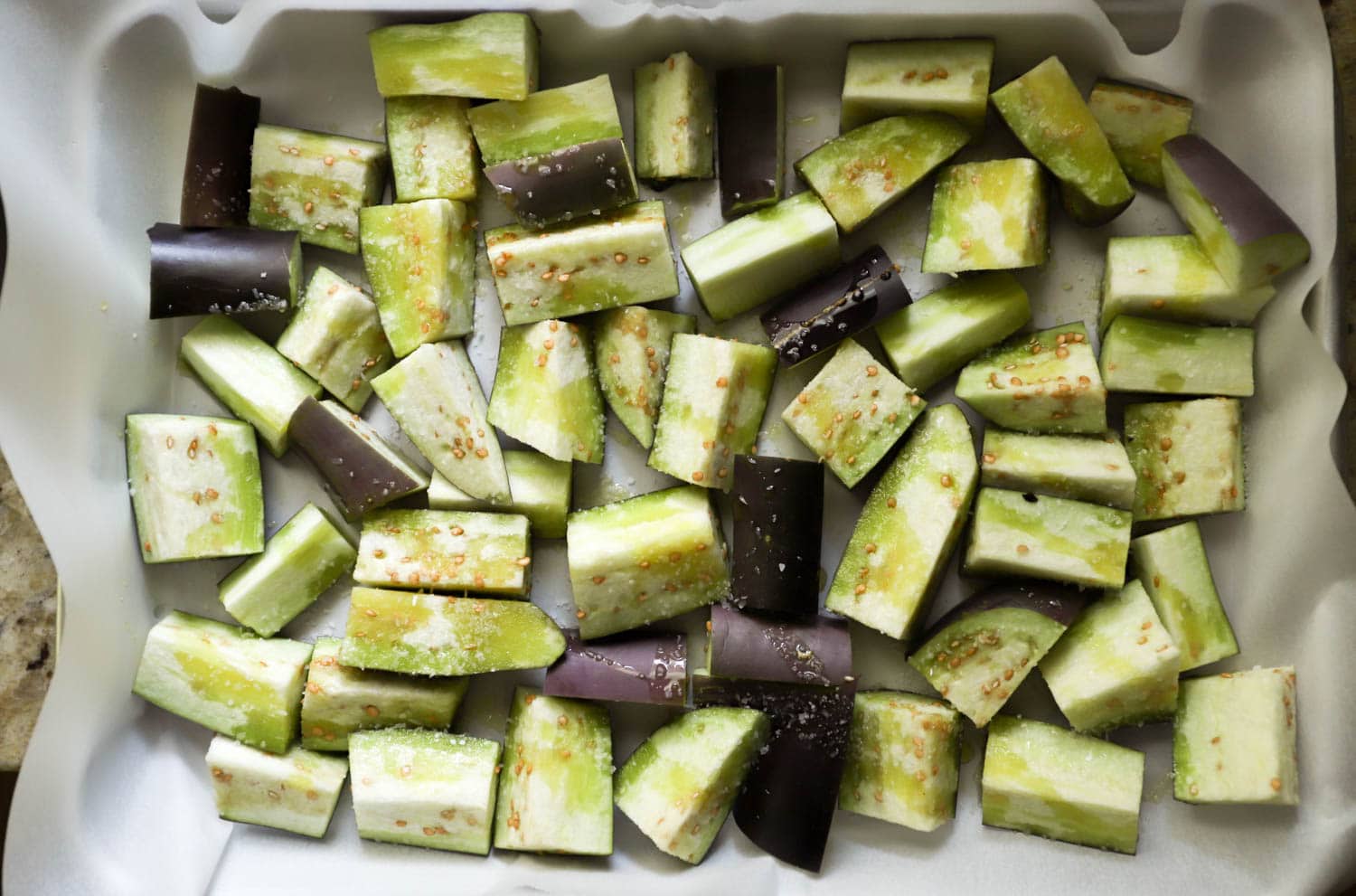 Raw eggplant on parchment paper cut into chunks.