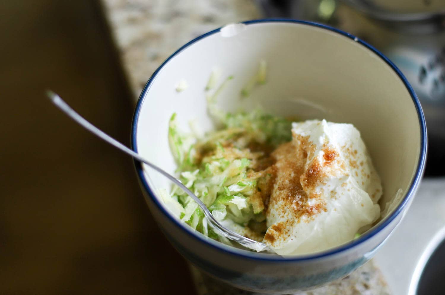 Bowl with yogurt sprinkled with sugar and grated cucumber.