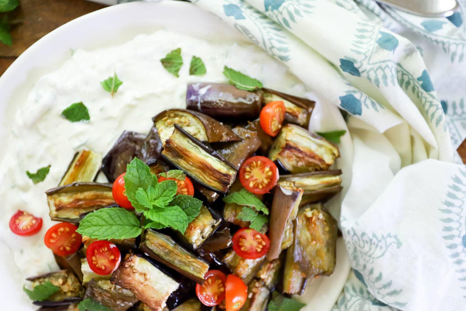 close up roasted eggplant plate topped with fresh mint and cherry tomatoes