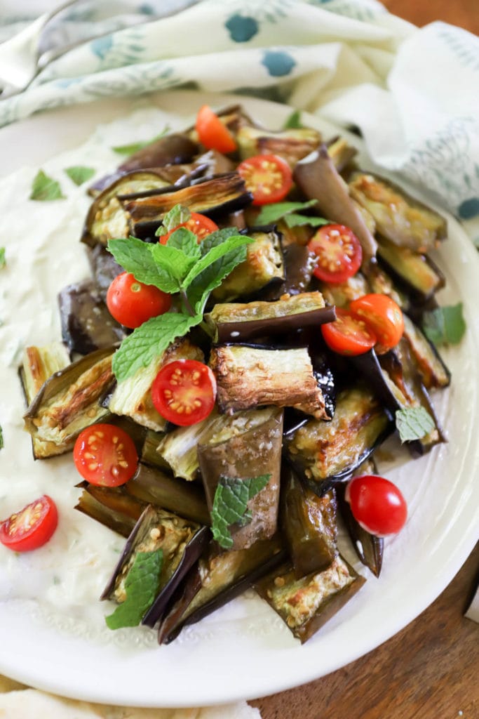 close up roasted eggplant plate topped with fresh mint and cherry tomatoes and decorative napkin