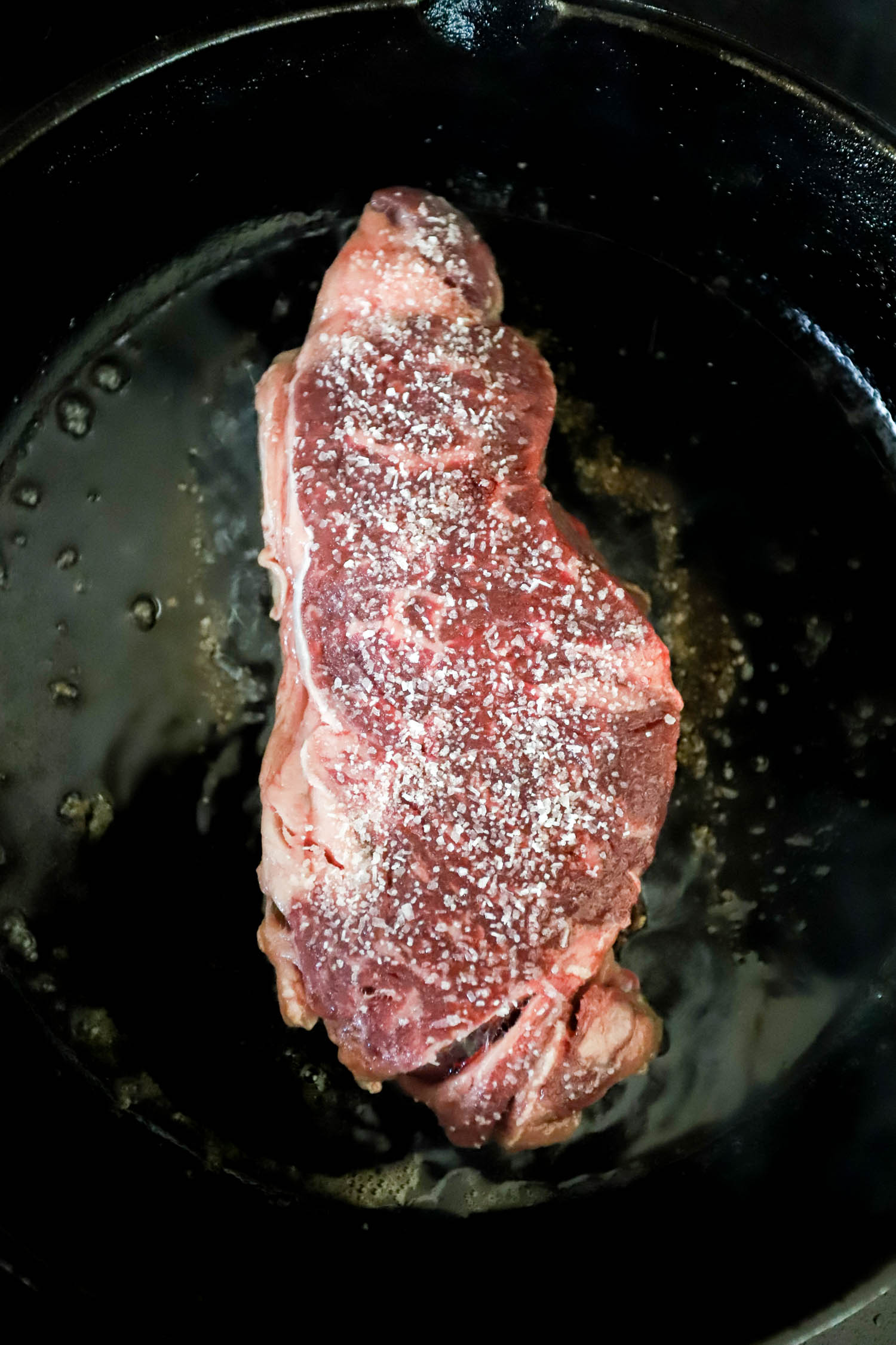 raw strip steak with salt in cast iron skillet