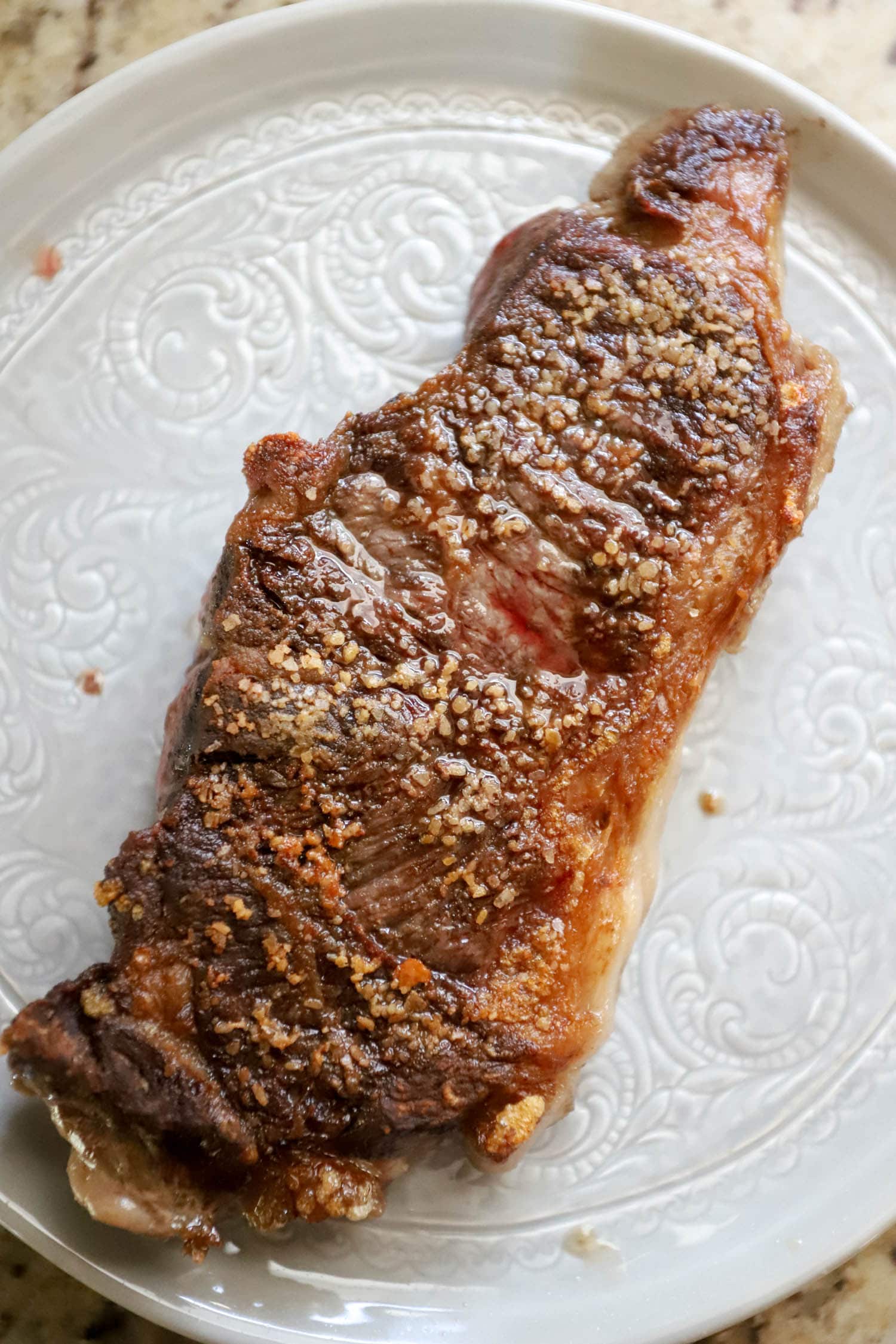 cooked strip steak on white plate resting