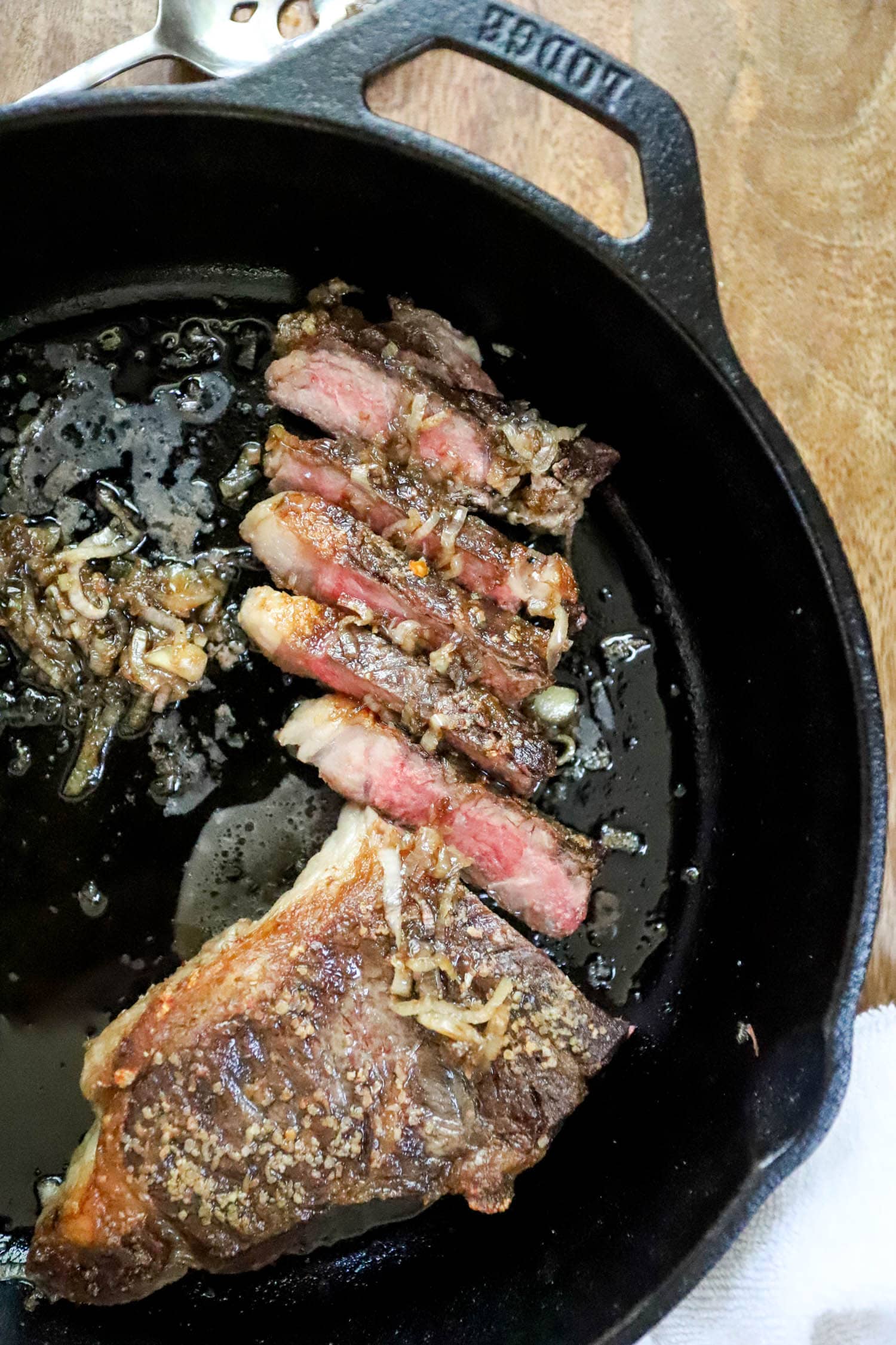 close up cast iron skillet with cooked sliced steak and shallot sauce over steak