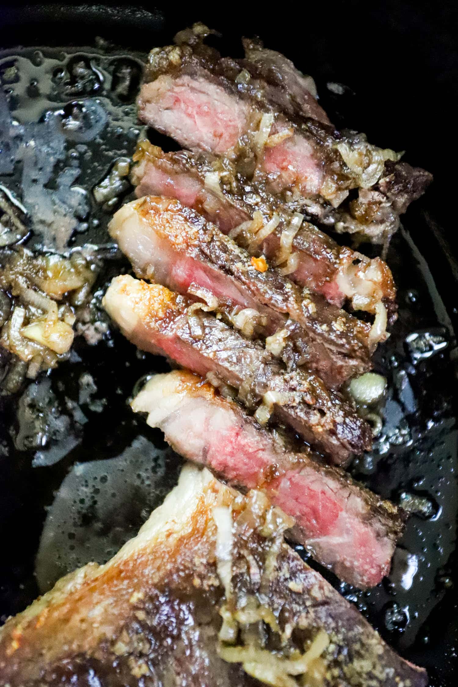 close up sliced rare steak with shallots on top