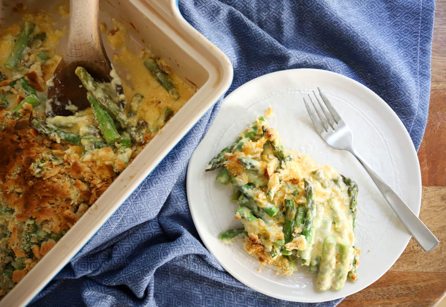 white plate with serving of cheesy baked asparagus on a blue napkin.