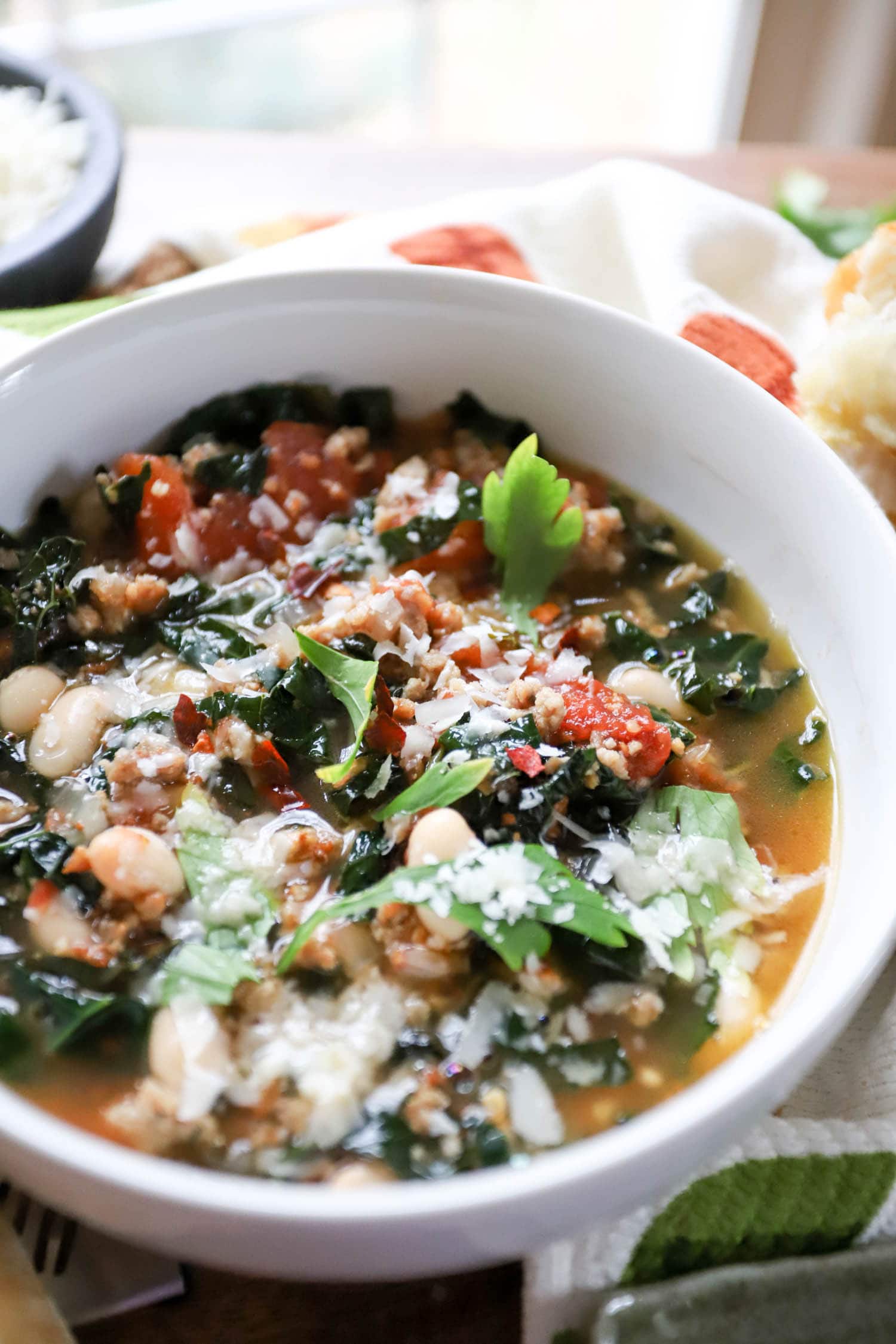 white bowl filled with sausage kale soup topped with parsley and parmesan flakes.