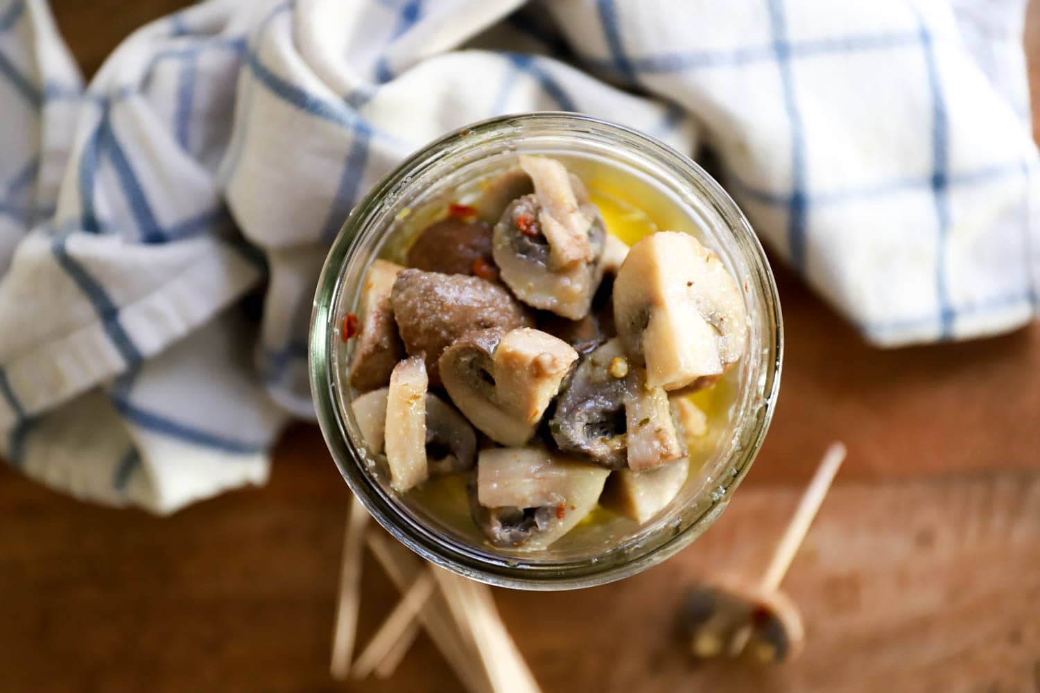 jar of pickled raw mushrooms with a blurry napkin in the background.