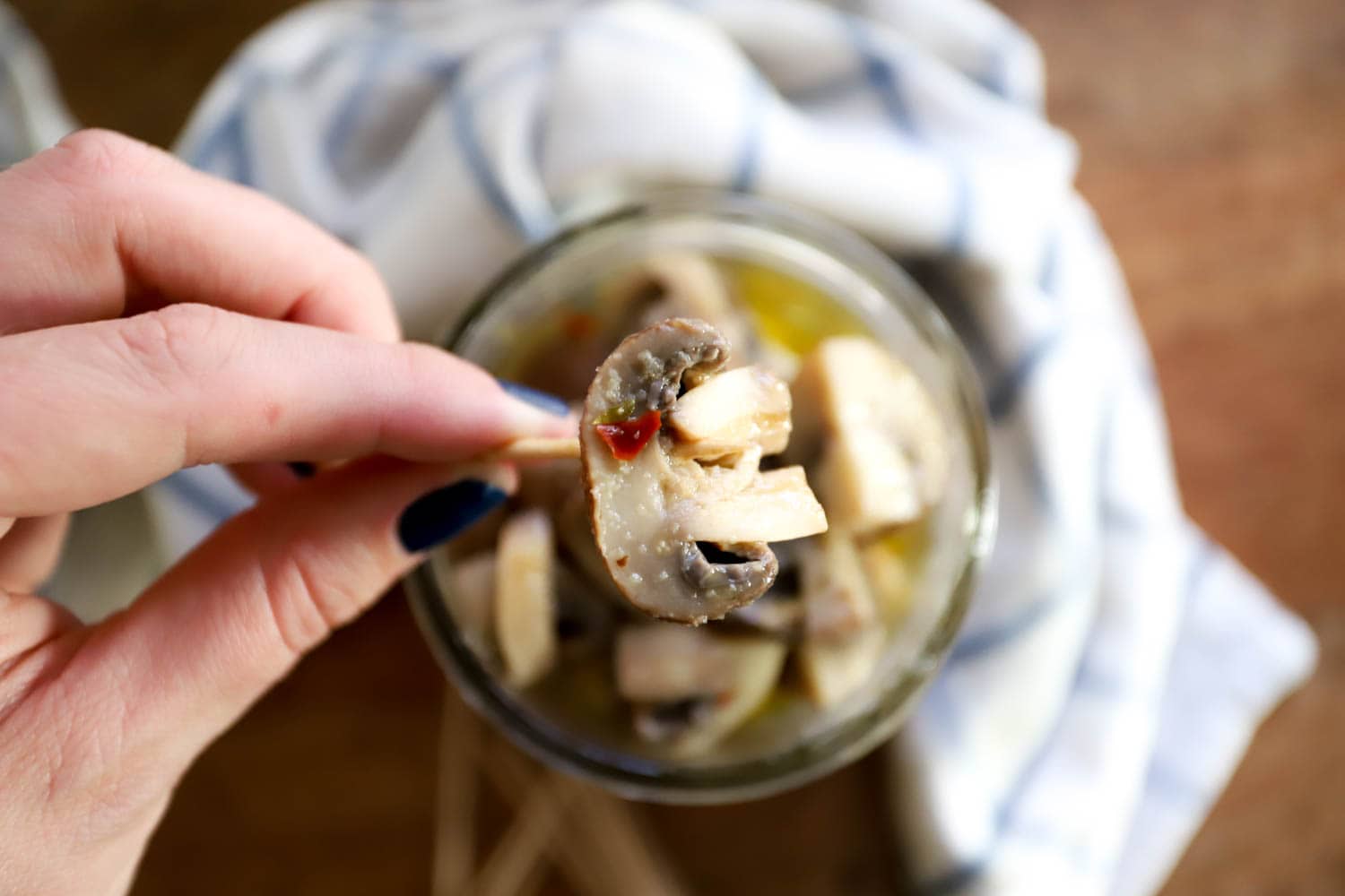 hand holding a marinated mushroom on a toothpick over open jar of mushrooms.